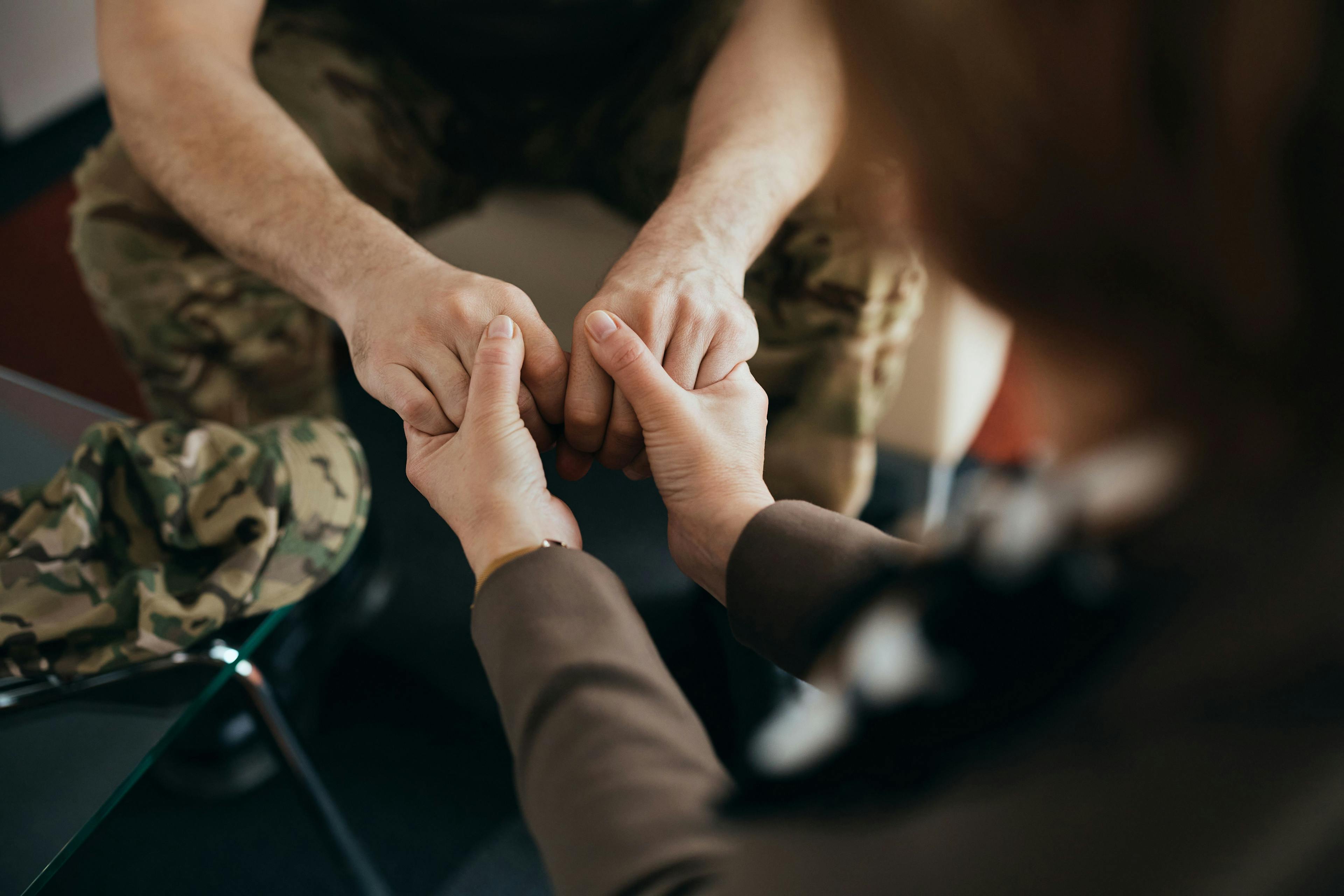 Close up of psychotherapist holding hands with soldier during counseling at her office - Image credit: Drazen | stock.adobe.com
