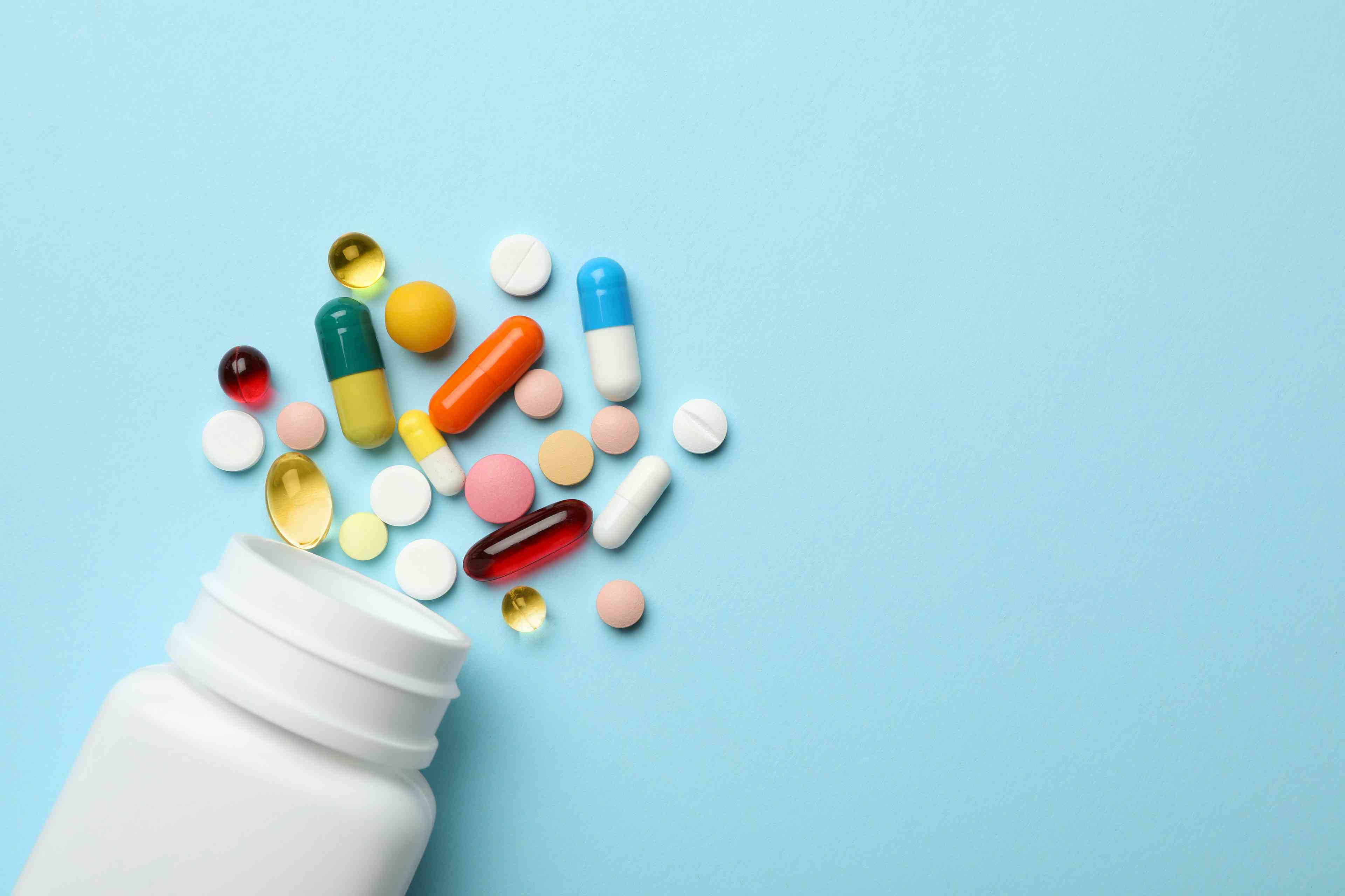 Bottle and scattered pills on color background, top view | Image Credit: New Africa - stock.adobe.com
