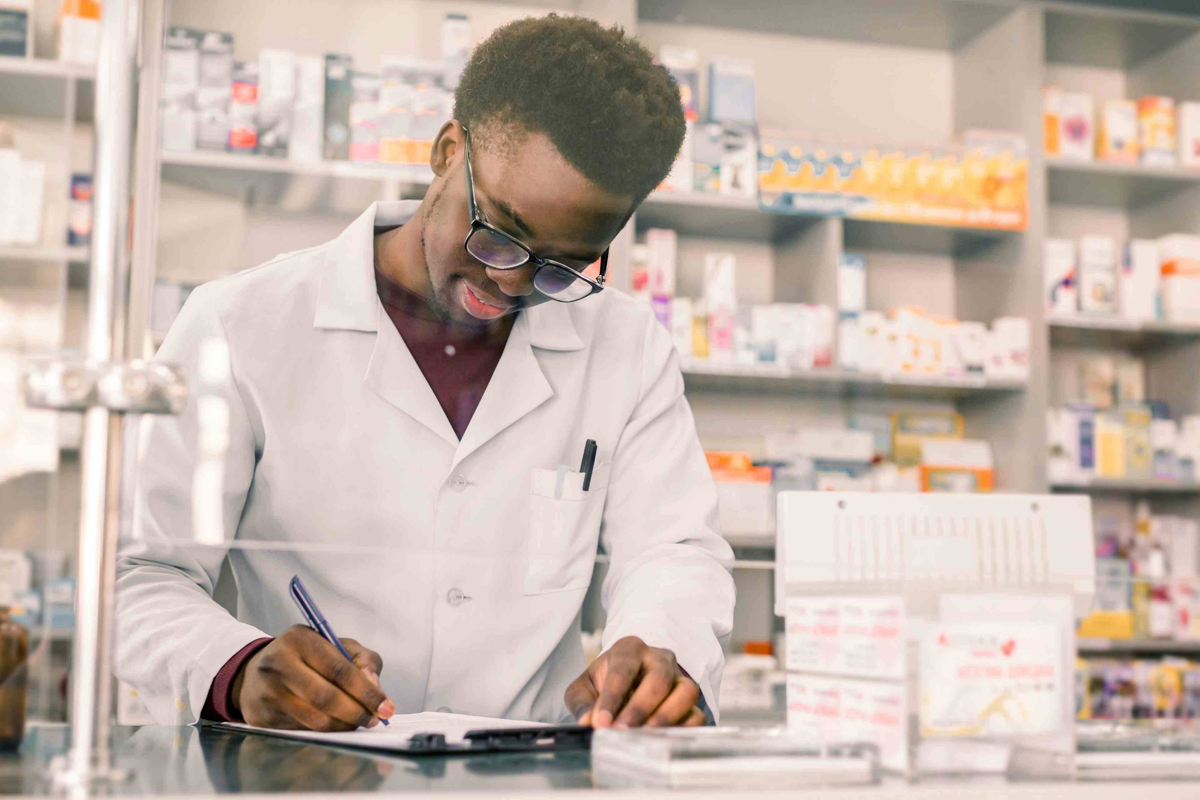 Portrait of a happy African American pharmacist writing prescription at workplace in modern pharmacy | Image Credit: sofiko14 - stock.adobe.com