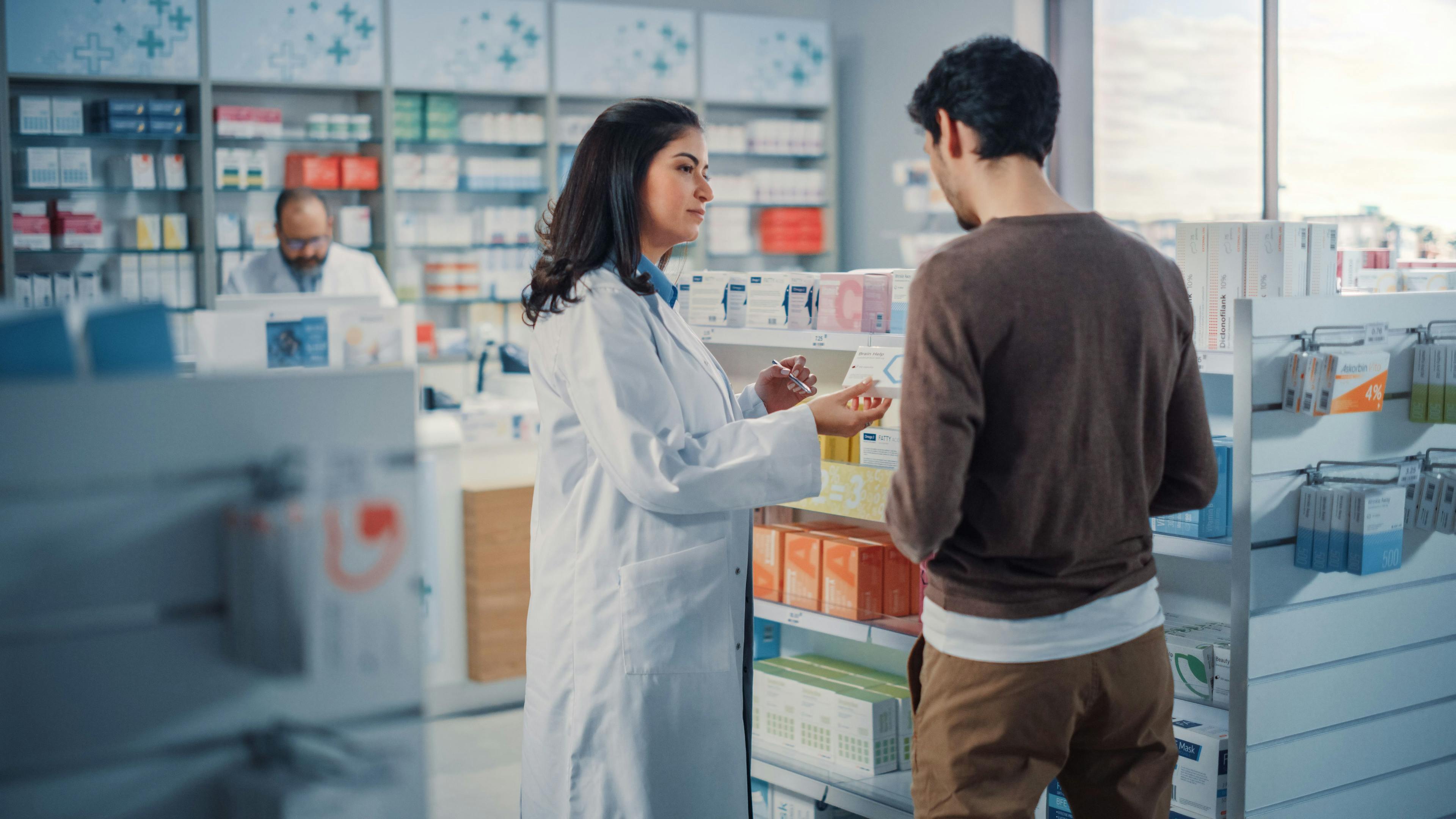 Pharmacy Drugstore: Hispanic Man Chooses to Buy Medicine, Drugs, Vitamins, Professional Female Pharmacist Helping Customer with Recommendation. Modern Pharma Store Shelves with Health Care