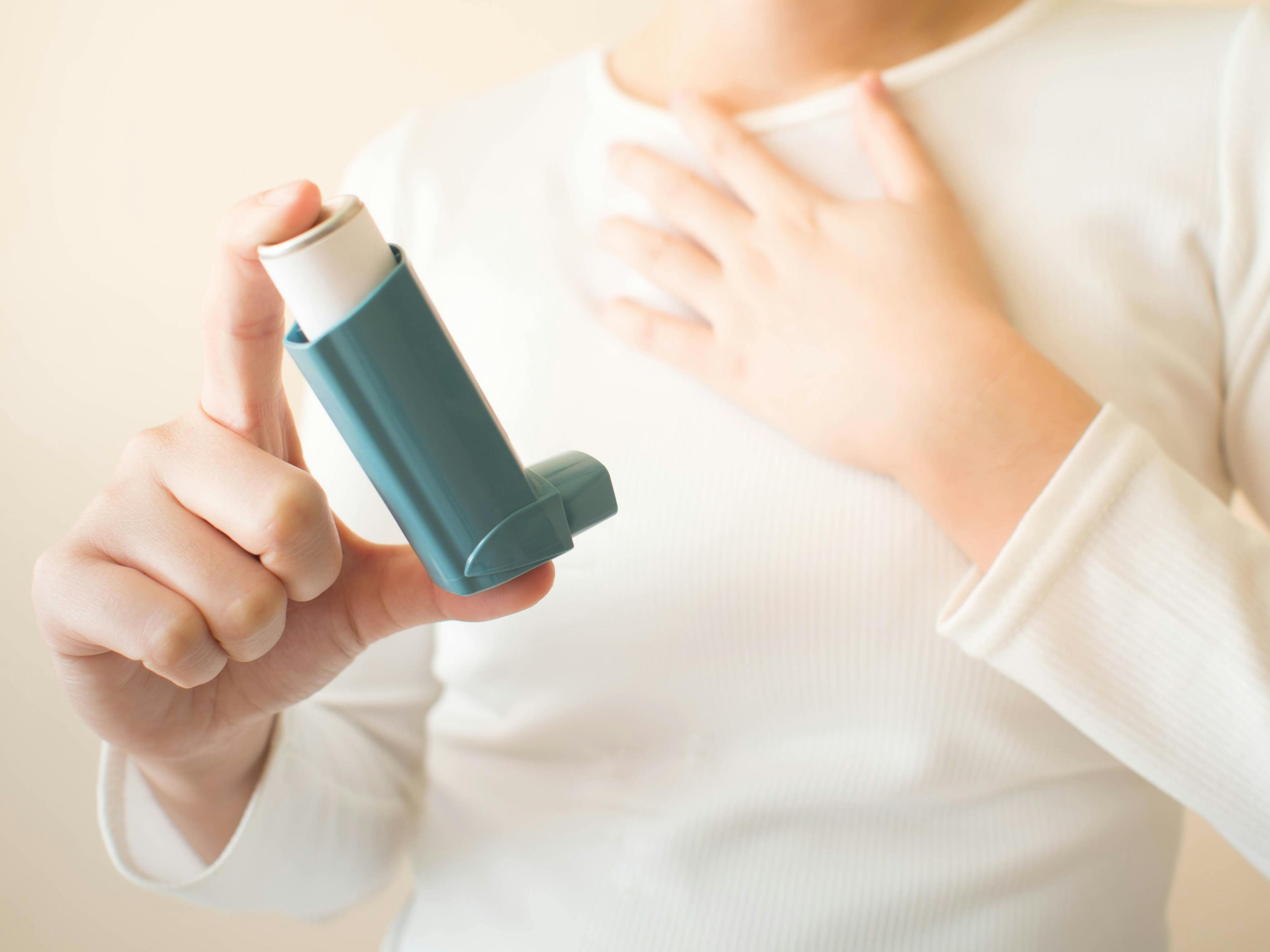Young female in white t-shirt using blue asthma inhaler for relief asthma attack. Pharmaceutical products is used to prevent and treat wheezing and shortness of breath caused asthma or COPD. Close up - Image credit: Orawan | stock.adobe.com