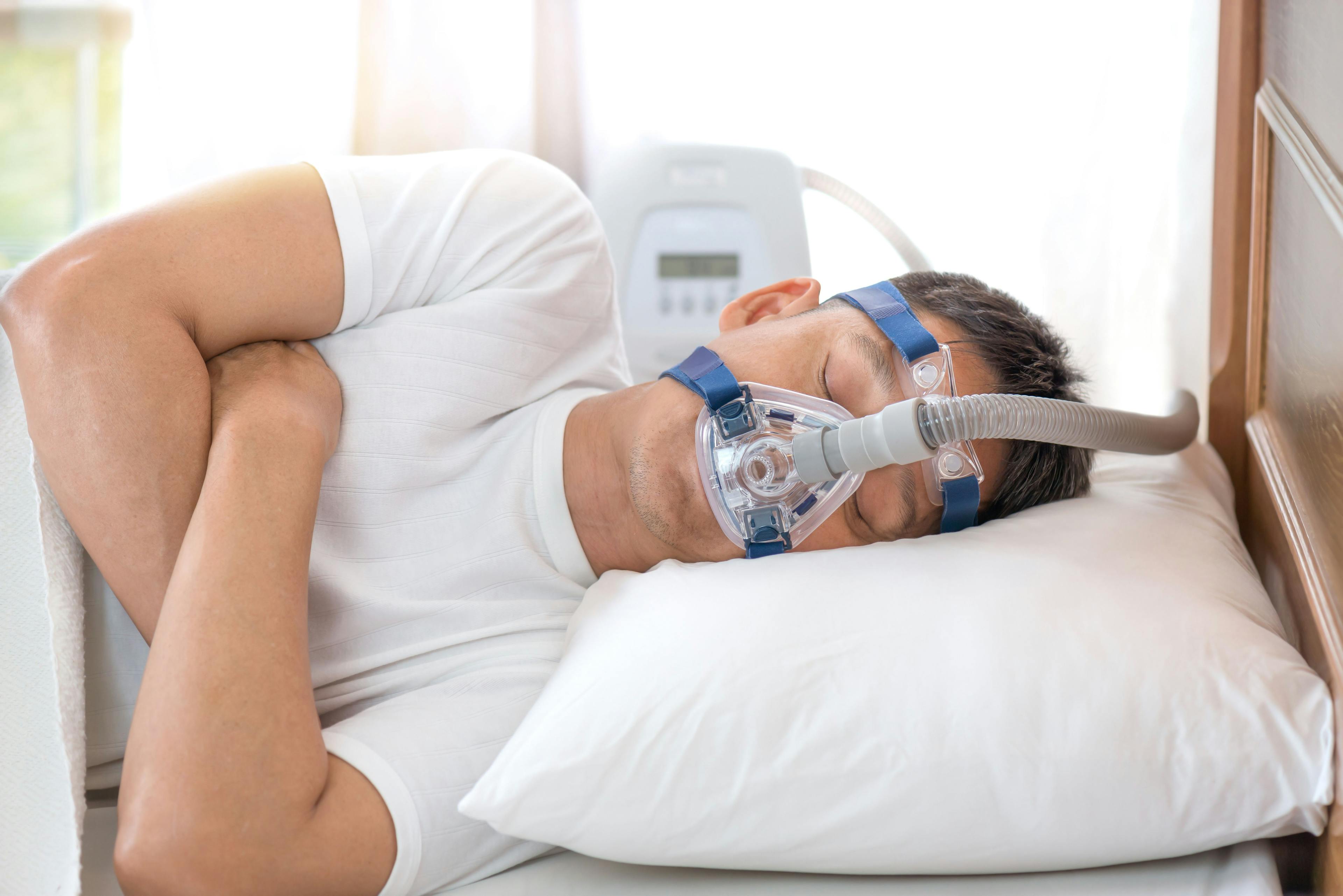 Man sleeping in bed wearing CPAP mask, sleep apnea therapy