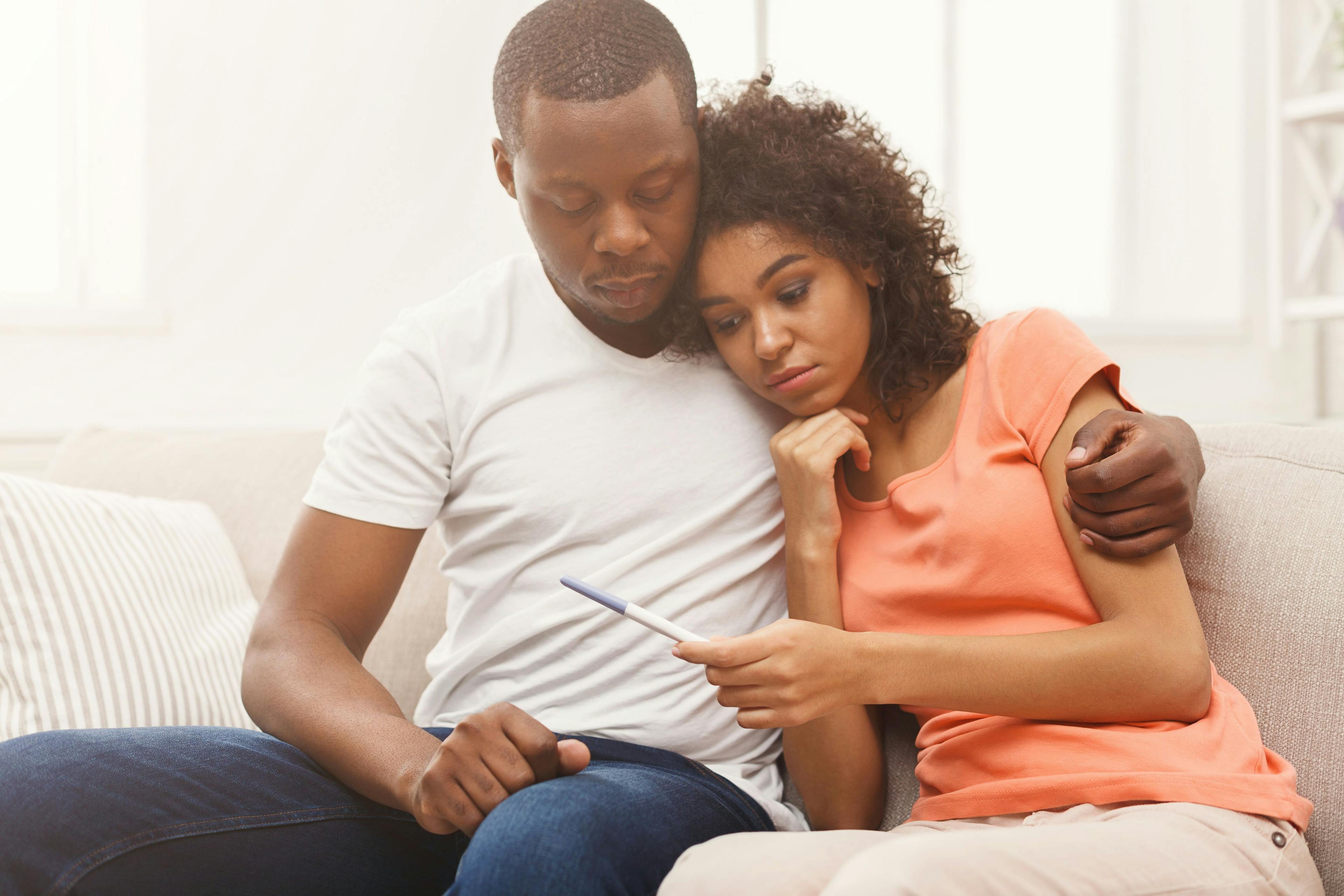 Sad couple sitting on a couch looking at a pregnancy test