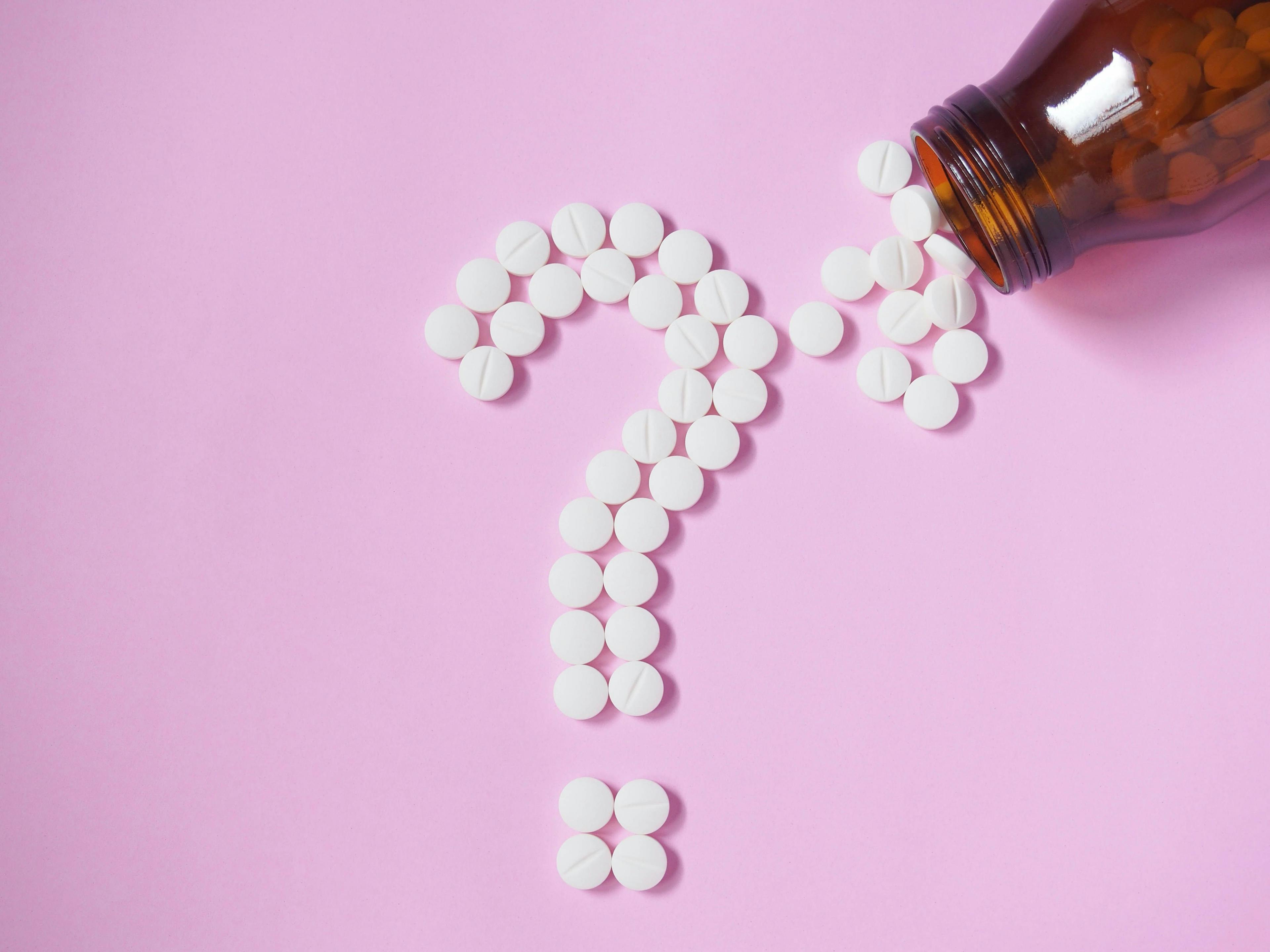 Question mark made by white pills spilling out of brown glass bottle on pink background | Image Credit: Orawan - stock.adobe.com