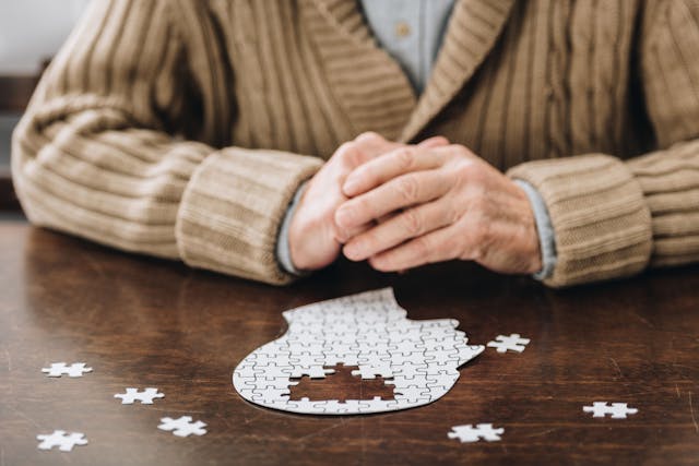 cropped view of senior man playing with puzzles on table. Dementia. | Image Credit: LIGHTFIELD STUDIOS - stock.adobe.com
