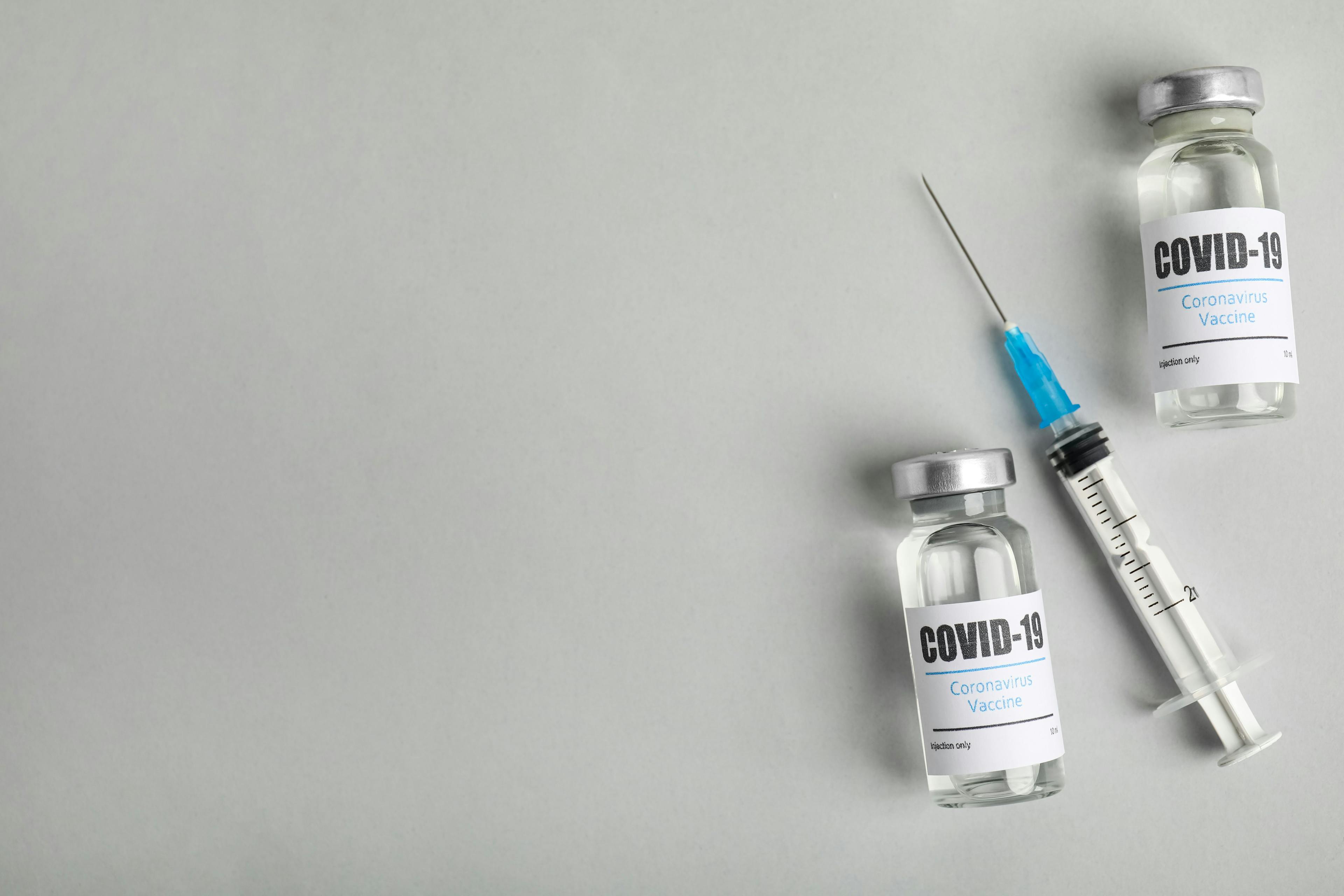 Vials with coronavirus vaccine and syringe on light background, flat lay. Space for text | Image credit: New Africa - stock.abobe.com 