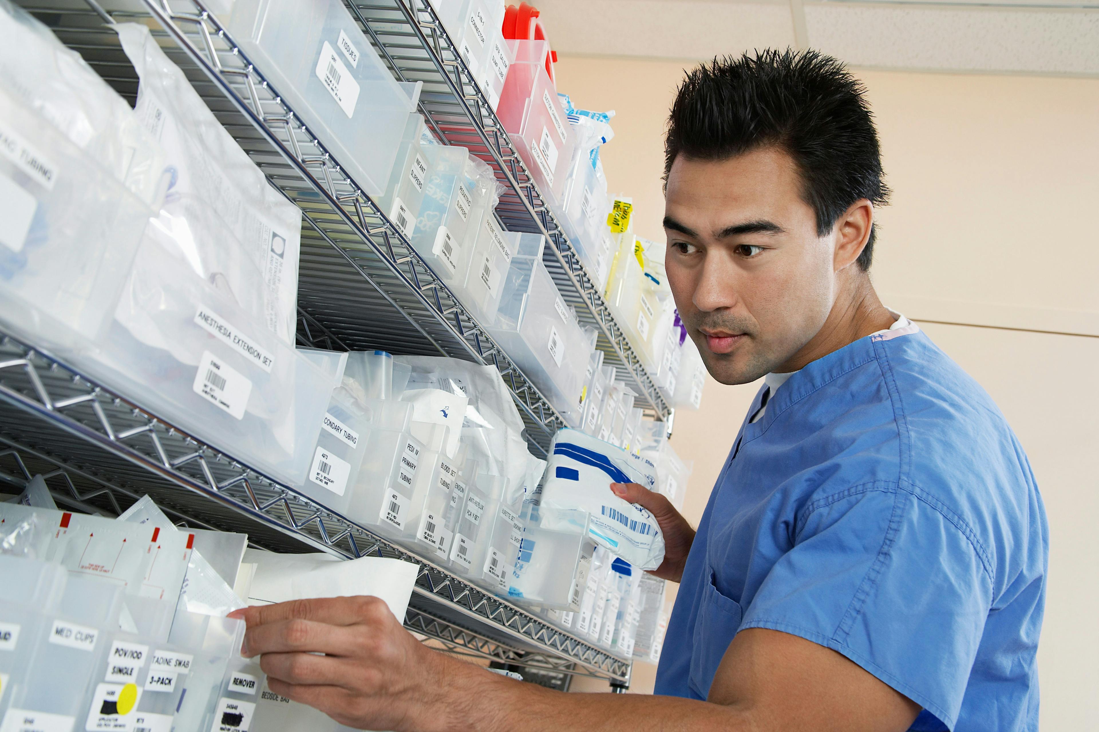 Young male nurse standing by shelves with medical supply