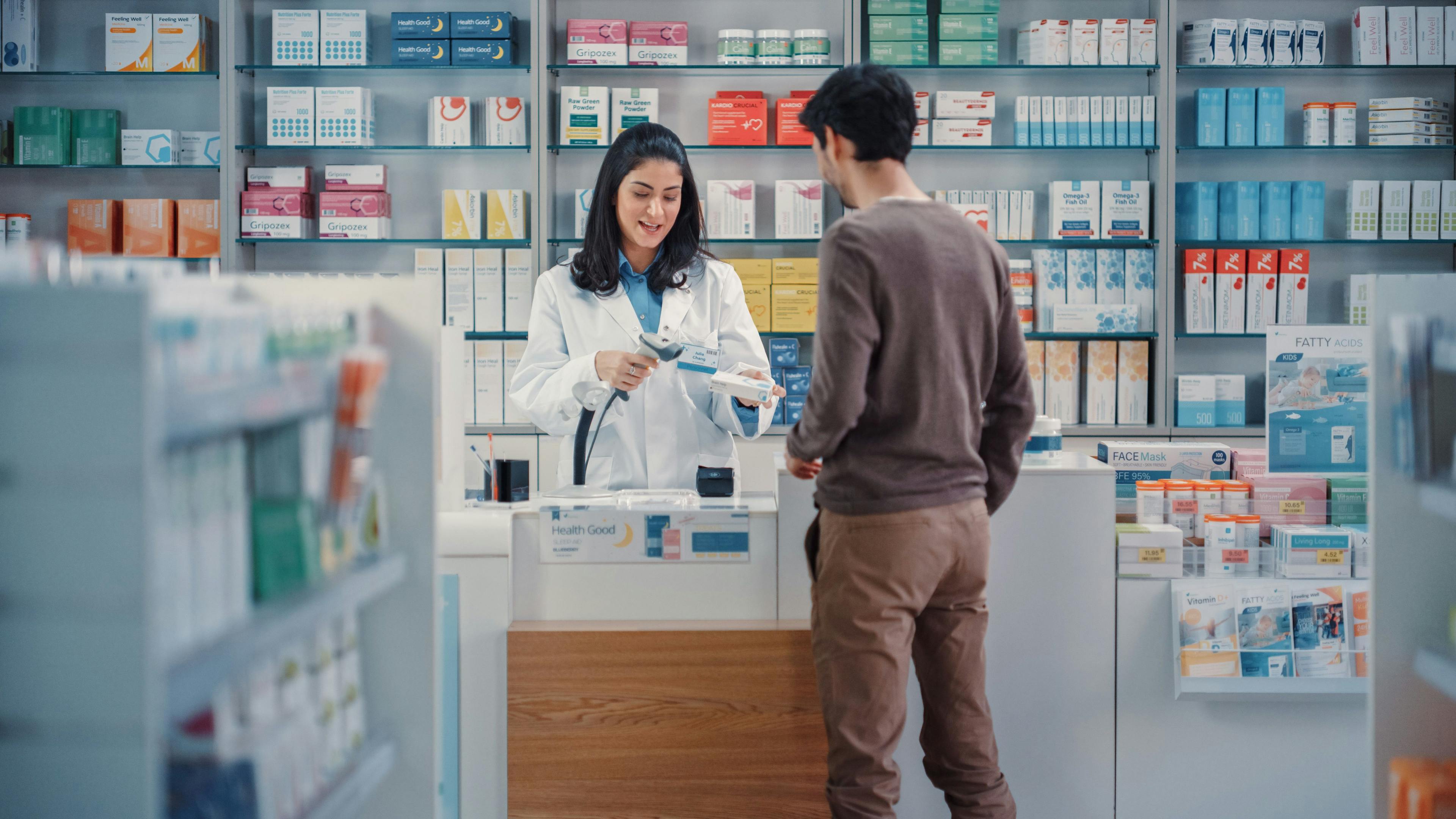 Pharmacy Drugstore Checkout Cashier Counter: Beautiful Female Pharmacist Scans Barcode and Handsome Young Man Talks to a Cashier and Pays for the Health Care Products at the Checkout Counter - Image credit: Gorodenkoff | stock.adobe.com
