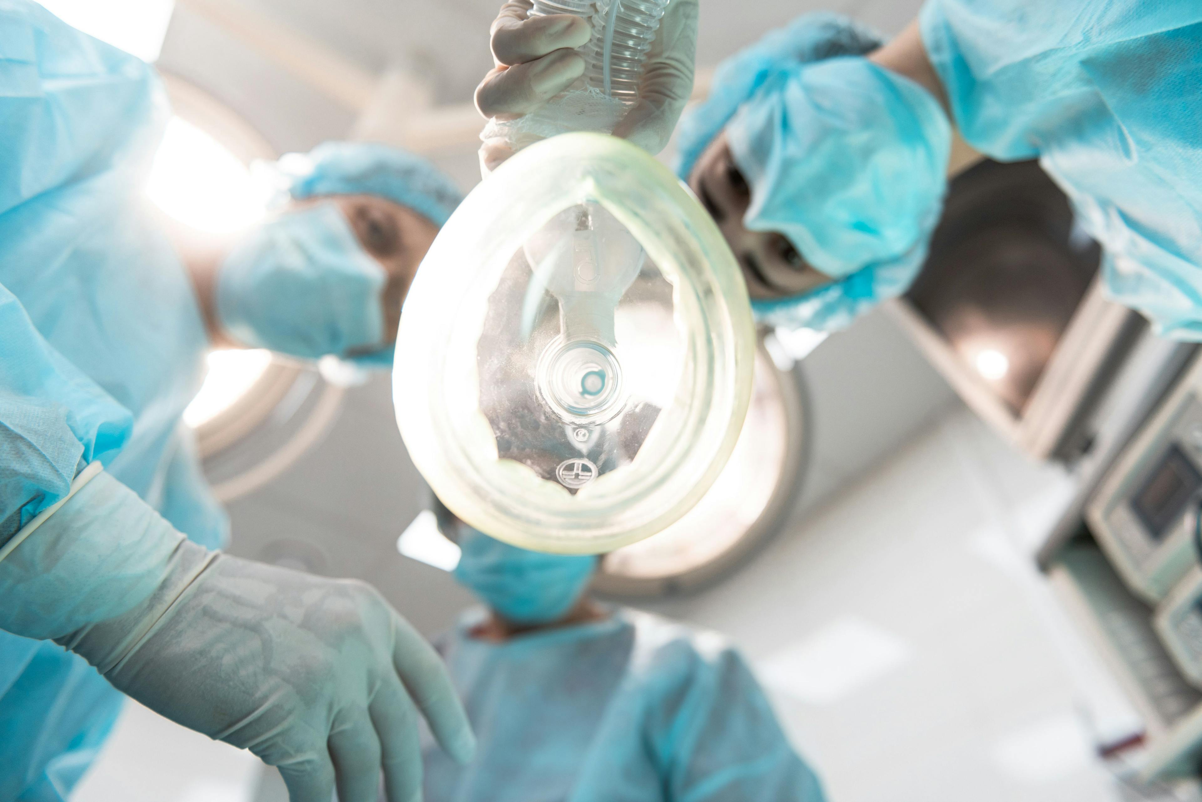 Bottom view of three professional doctors leaning over the patient and wearing medical masks while holding the anesthetic inhaler - Image credit: Yakobchuk Olena | stock.adobe.com