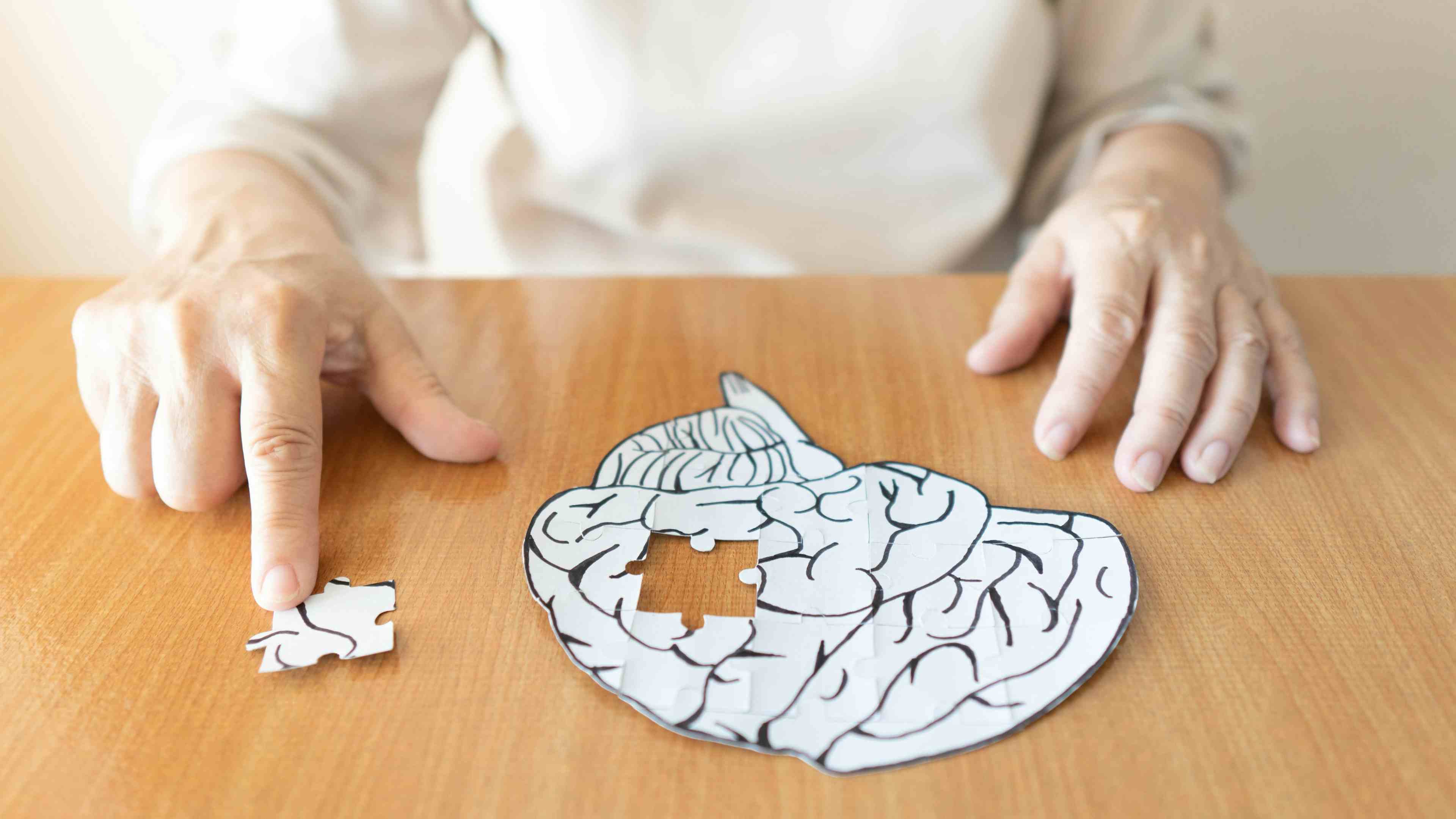 Elderly woman hands putting missing white jigsaw puzzle piece down into the place as a human brain shape | Image credit: Orawan - stock.adobe.com