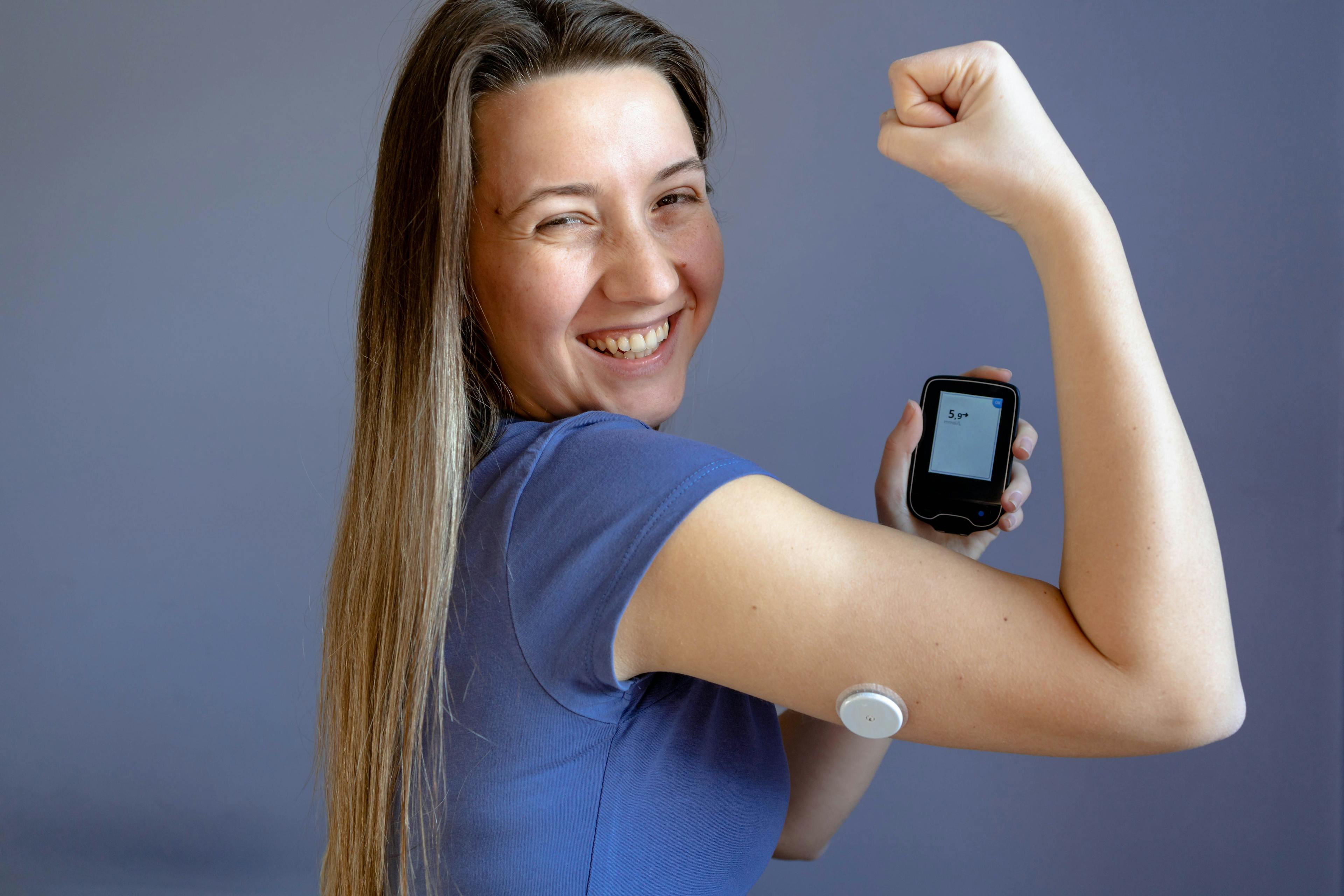 Woman smiling and showing her arm with a continuous glucose monitor for diabetes