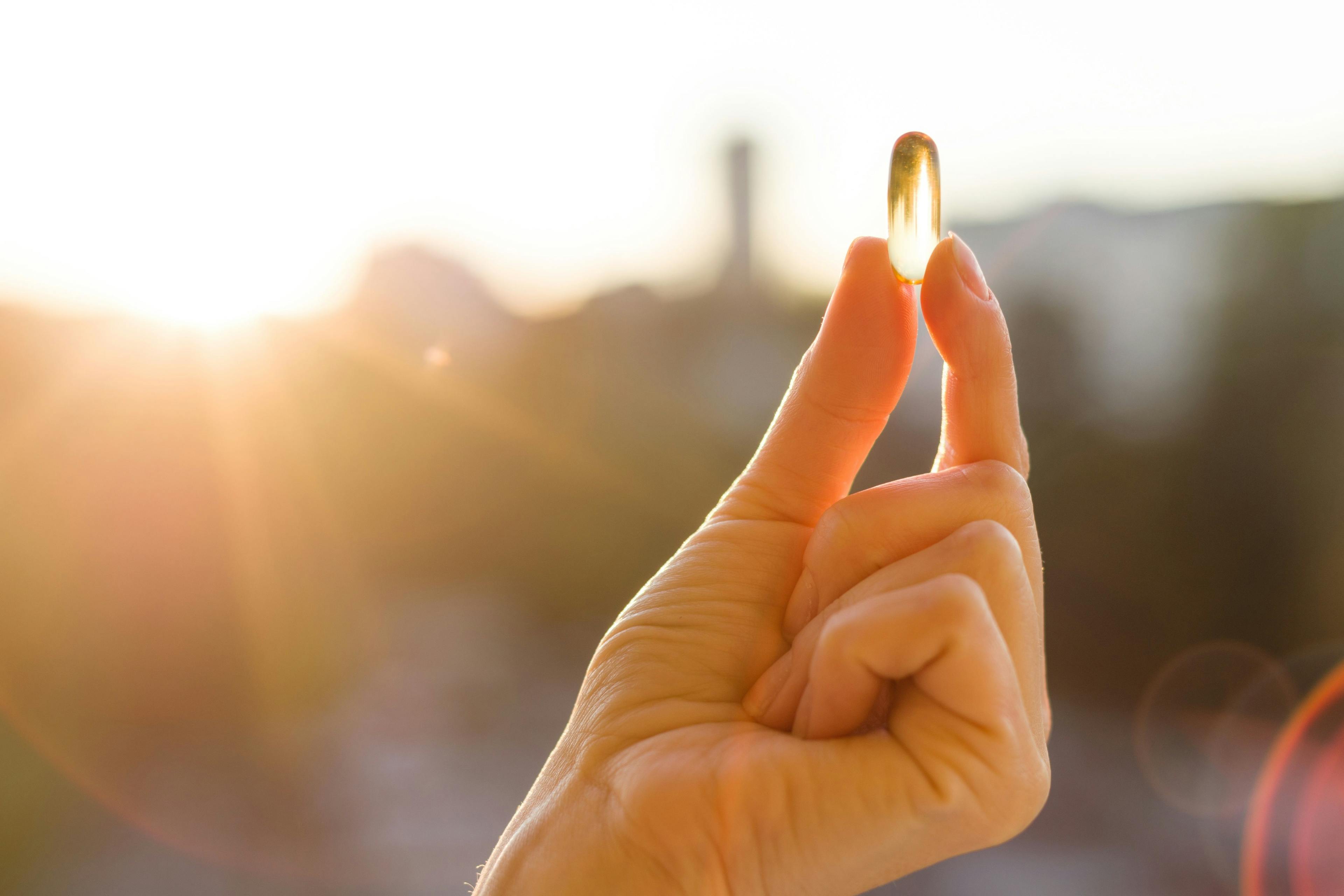 Hand of a woman holding fish oil Omega-3 capsules, urban sunset background. Healthy eating, medicine, health care, food supplements and people concept | Image Credit: Valerii Honcharuk - stock.adobe.com