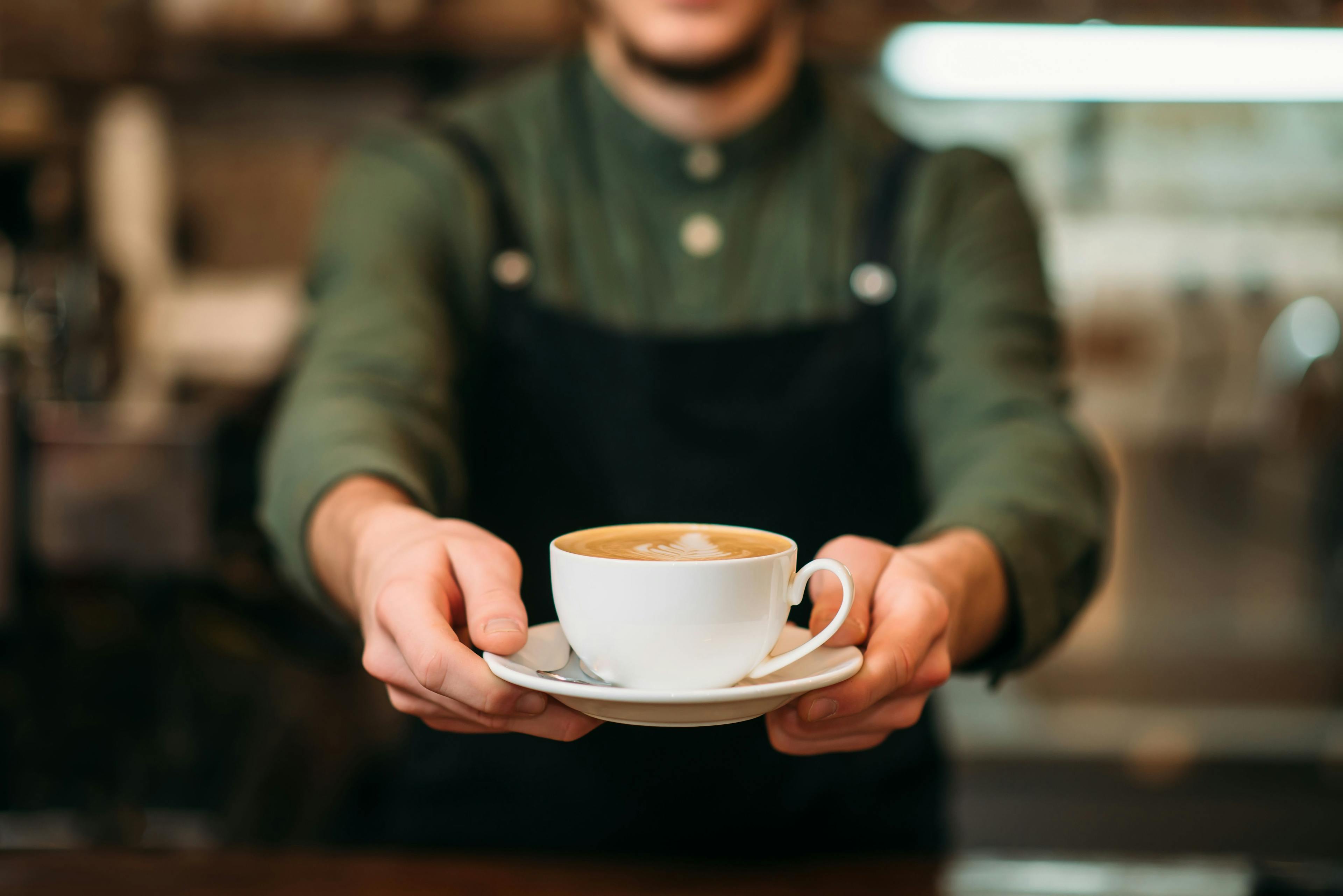 Waiter in black apron stretches a cup of coffee | Image credit: Omad_Soul - stock.adobe.com