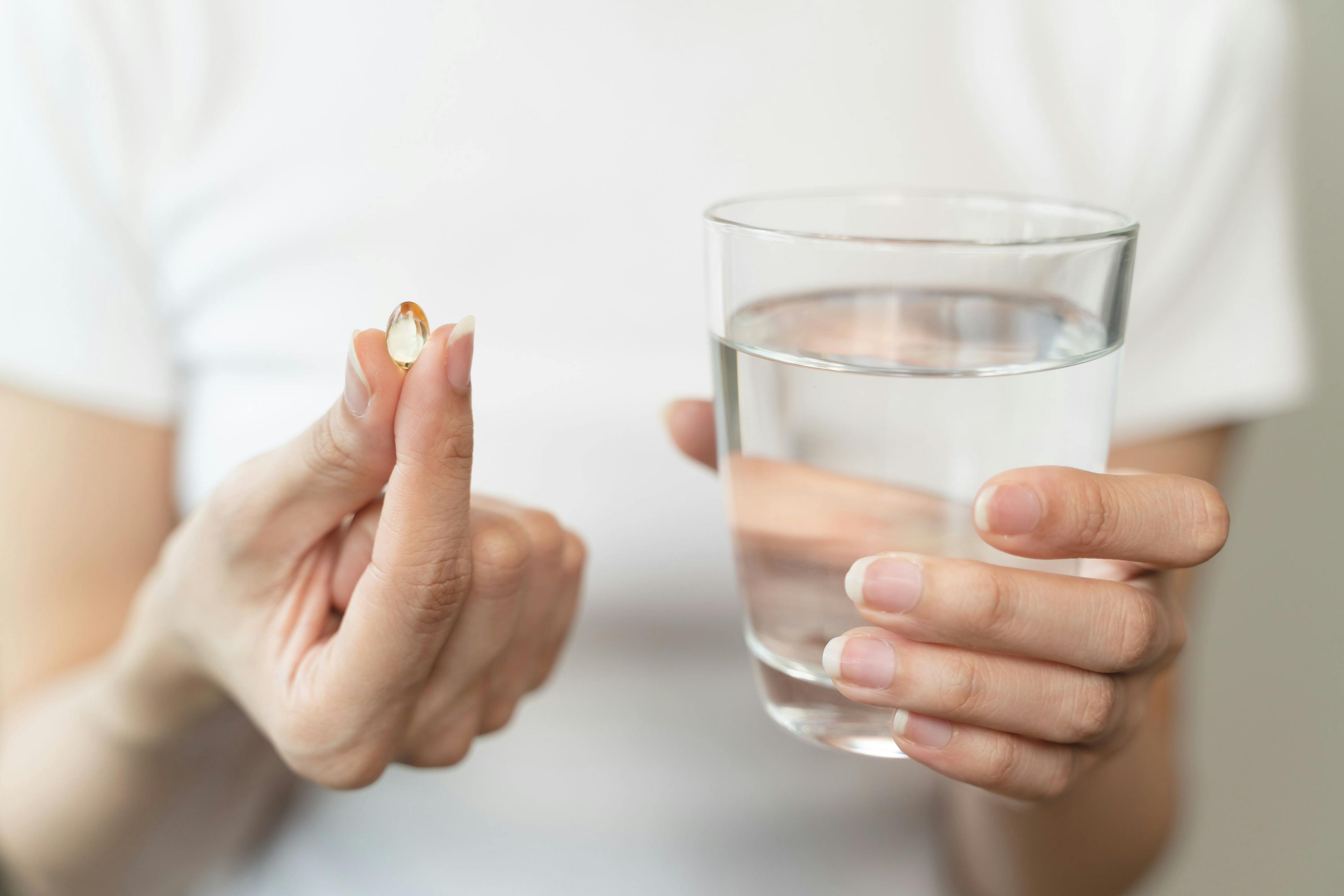 Adult taking a multivitamin with water -- Image credit: Pormezz | stock.adobe.com