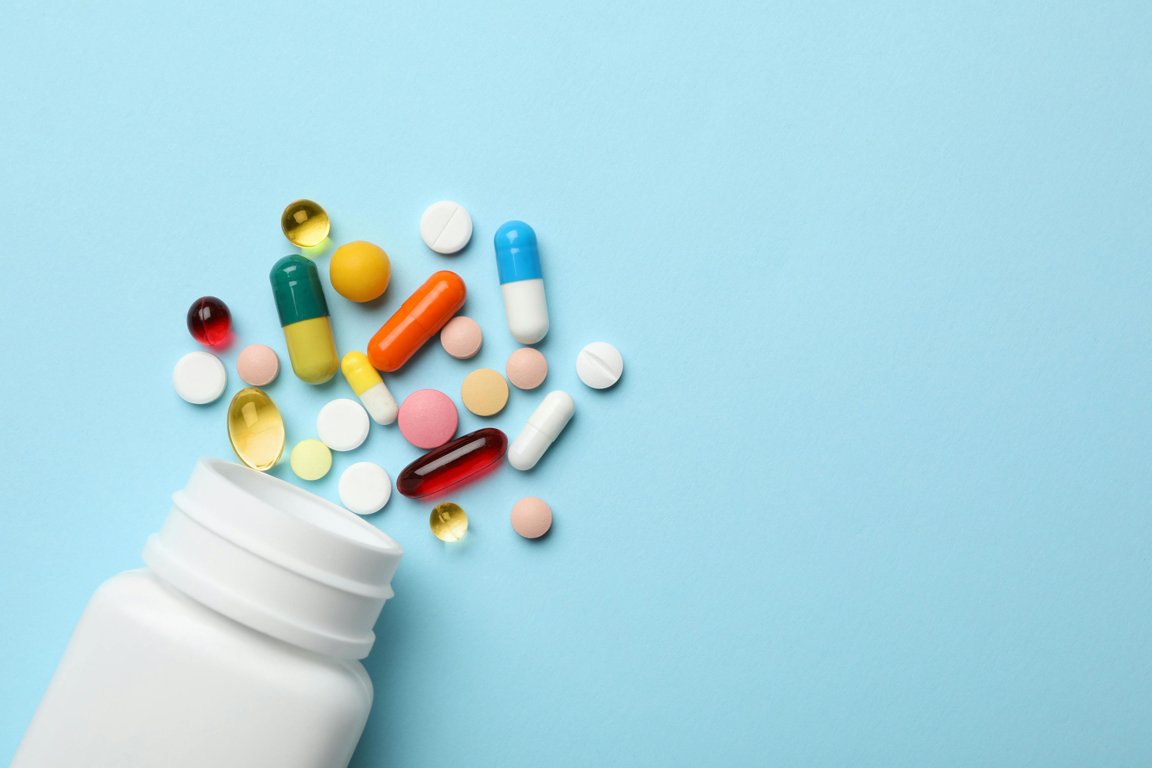 Bottle and scattered pills on blue backdrop | Image credit: New Africa - stock.adobe.com