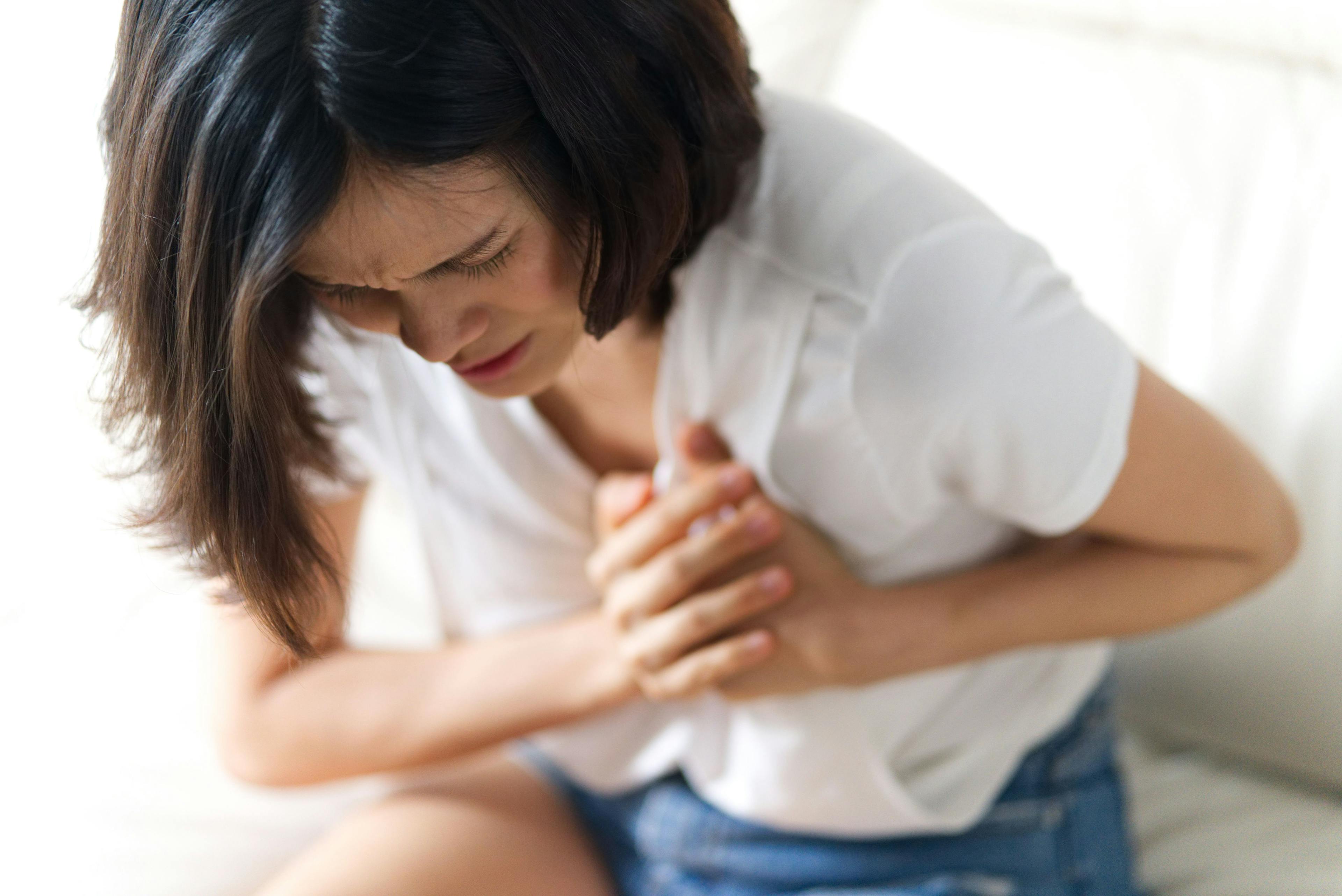 Unwell condition and sickness concept; Asian woman having heart attack sitting on sofa. She puts both hand on her left chest feeling painful and need emergency medical assistance | Image credit: Kawee - stock.adobe.com