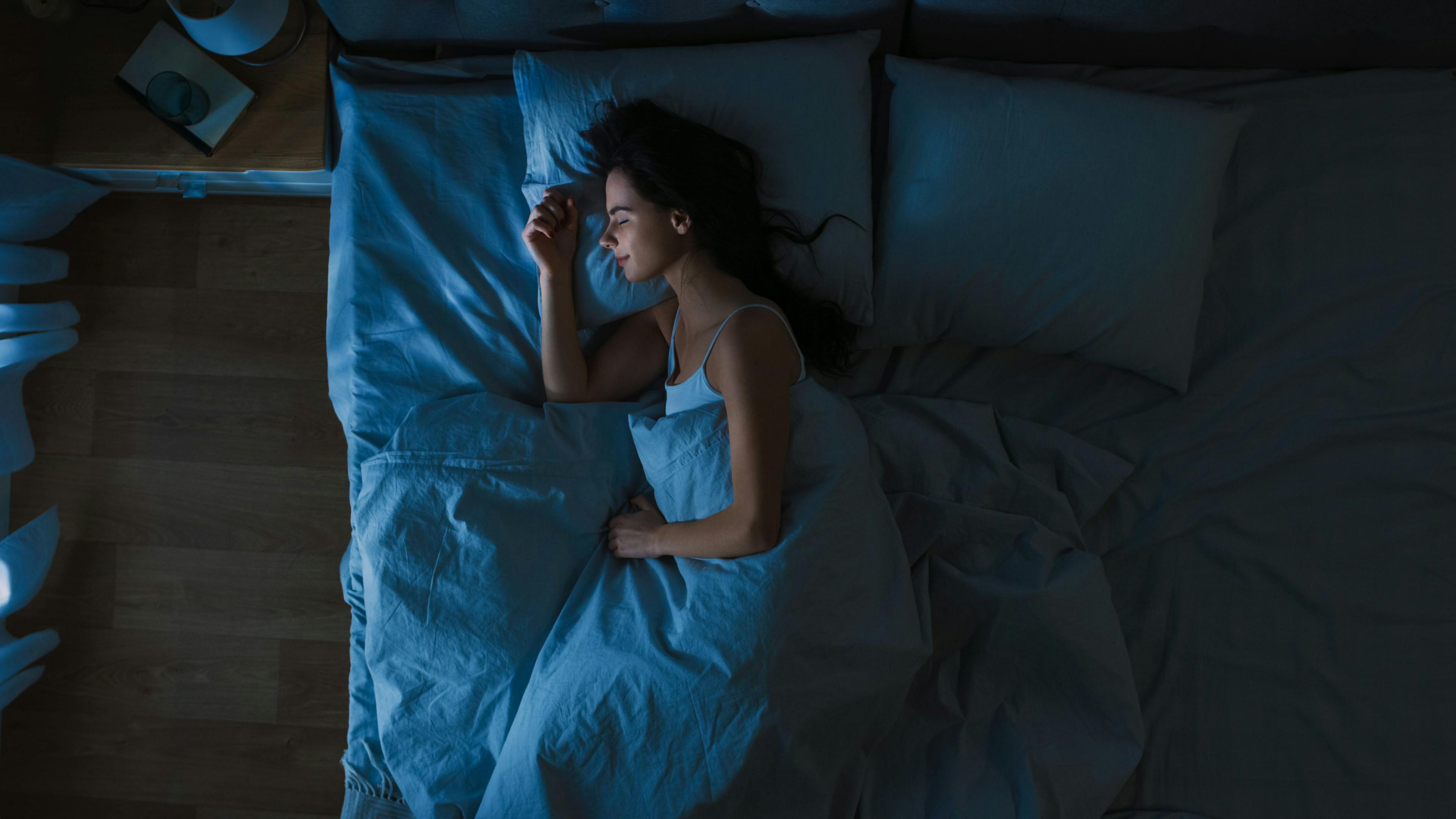 Top View of Young Woman Sleeping Cozily on a Bed in Bedroom at Night