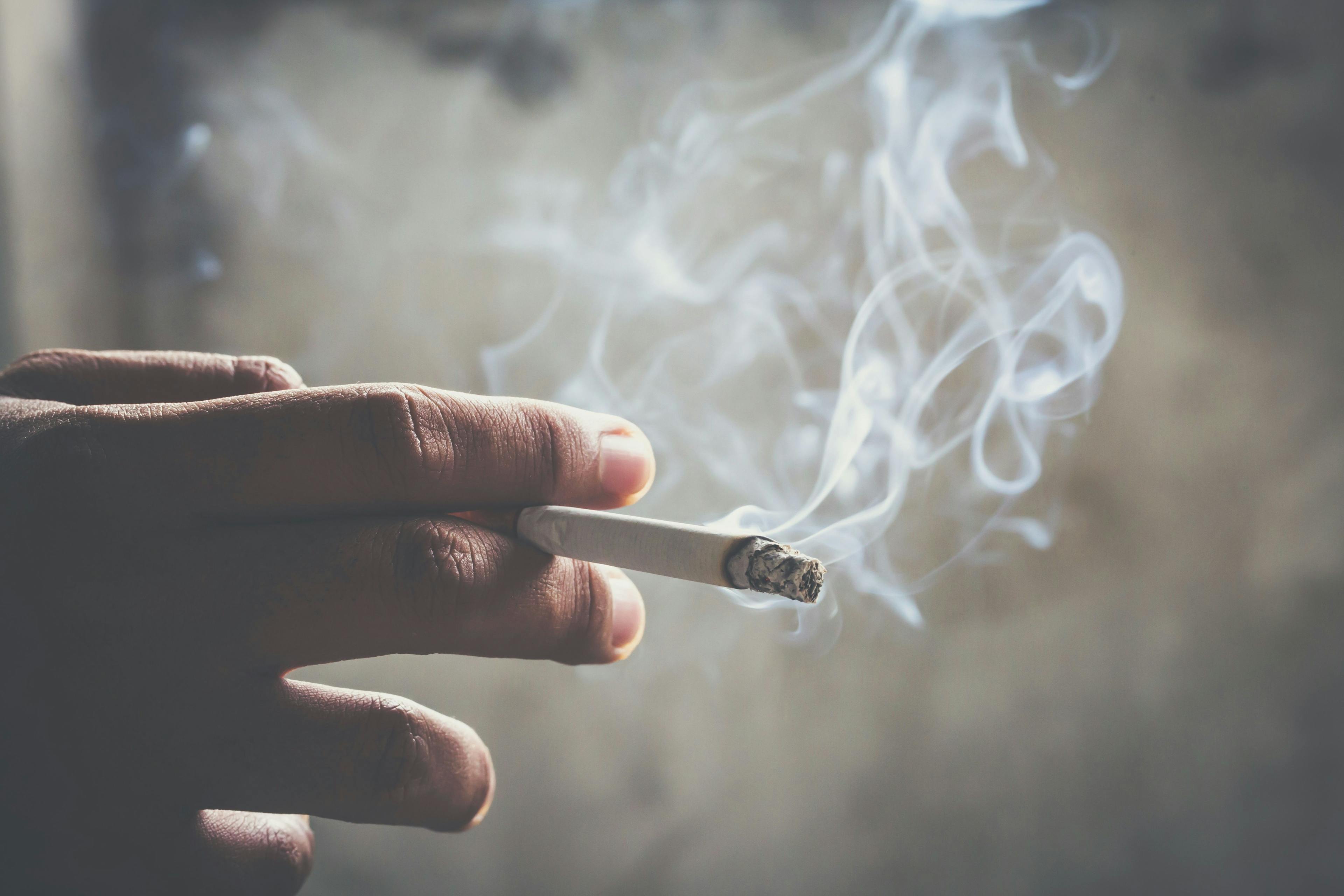 man holding smoking a cigarette in hand. Cigarette smoke spread. dark background - Image credit: Methaphum | stock.adobe.com
