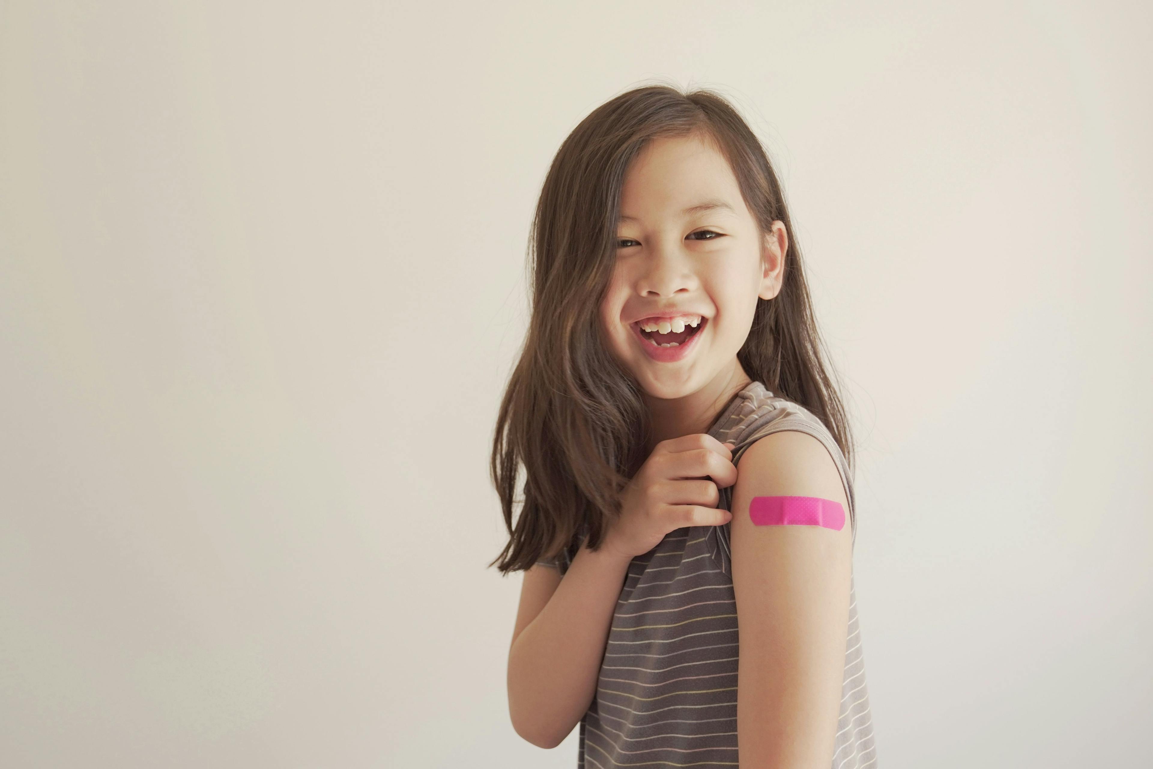 Mixed Asian young girl showing her arm with pink bandage after got vaccinated or inoculation, child immunization, covid omicron vaccine concept | Image Credit: SewcreamStudio - stock.adobe.com