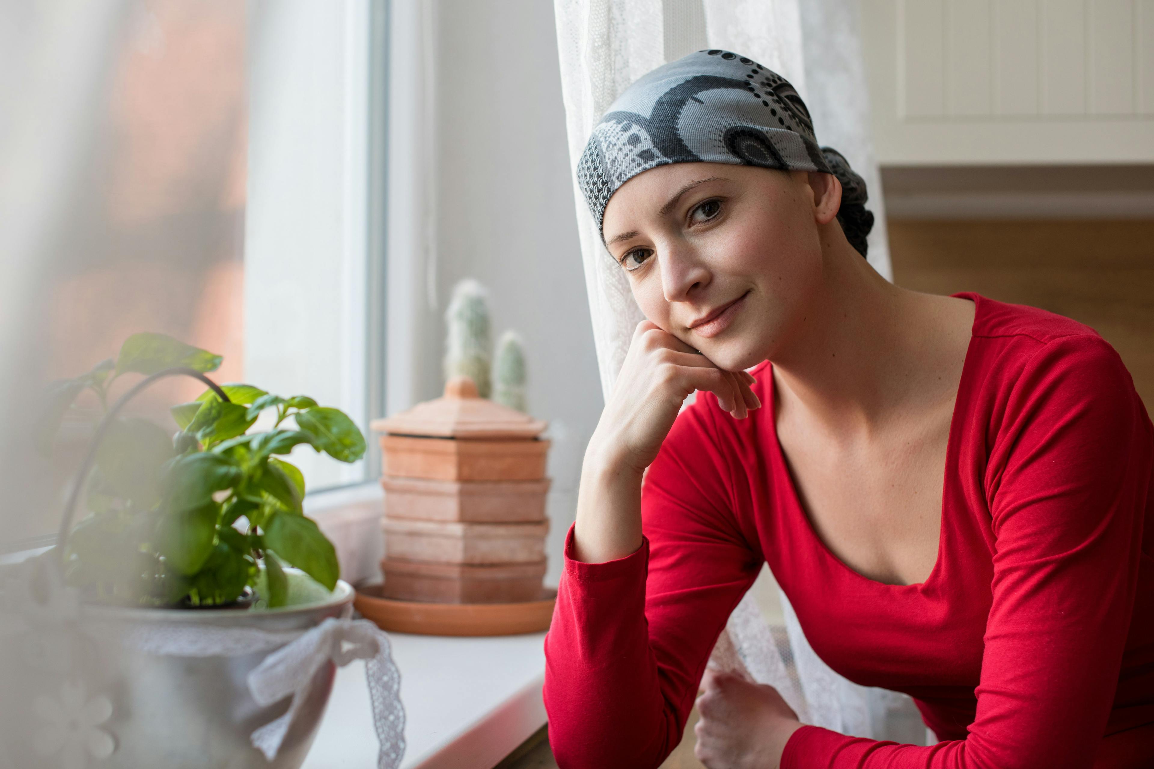Young positive adult female cancer patient sitting in the kitchen by a window, smiling and looking at the camera. Credit: andreaobzerova - stock.adobe.com
