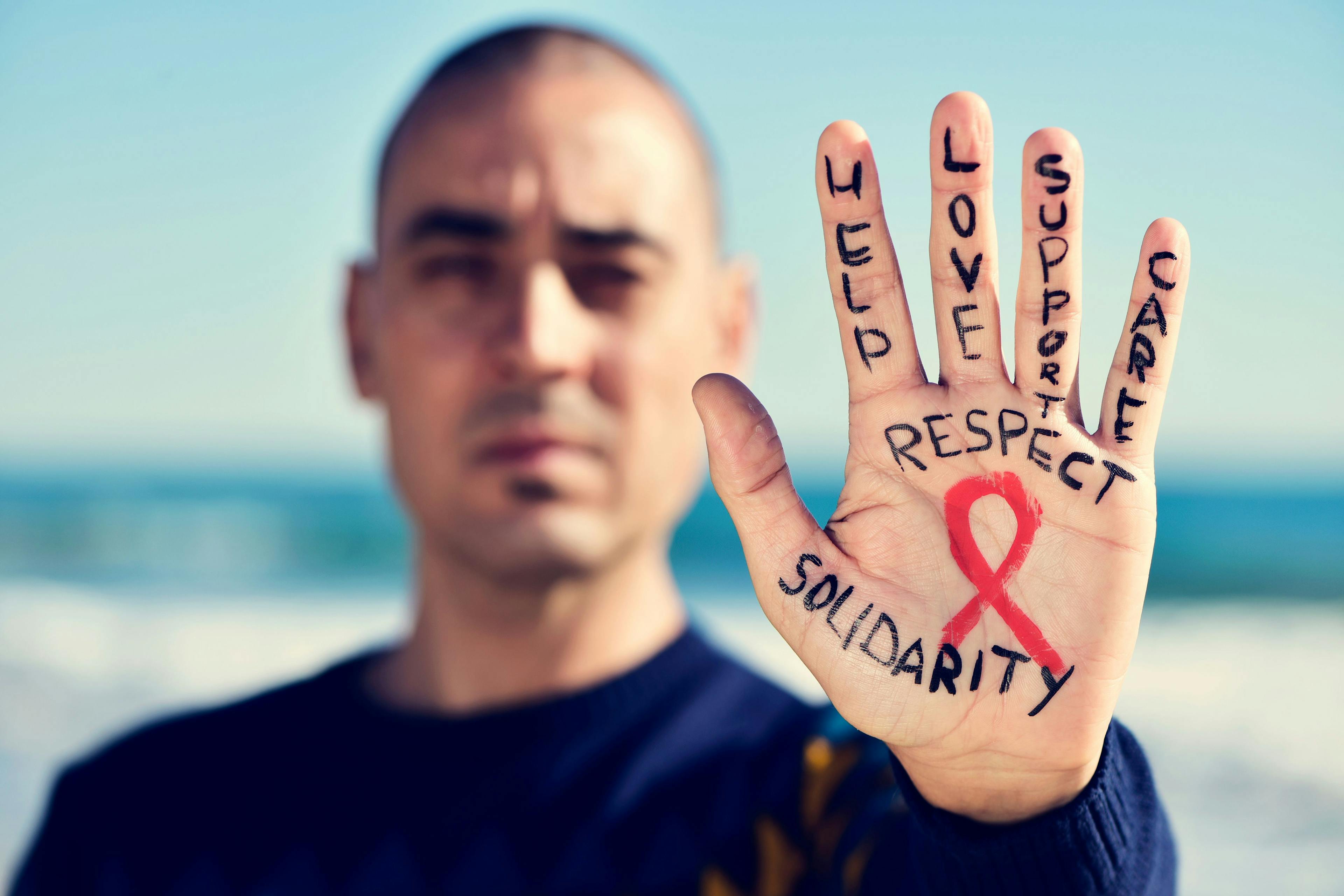 Young man with a red ribbon for the fight against AIDS in his hand. Credit: nito - stock.adobe.com
