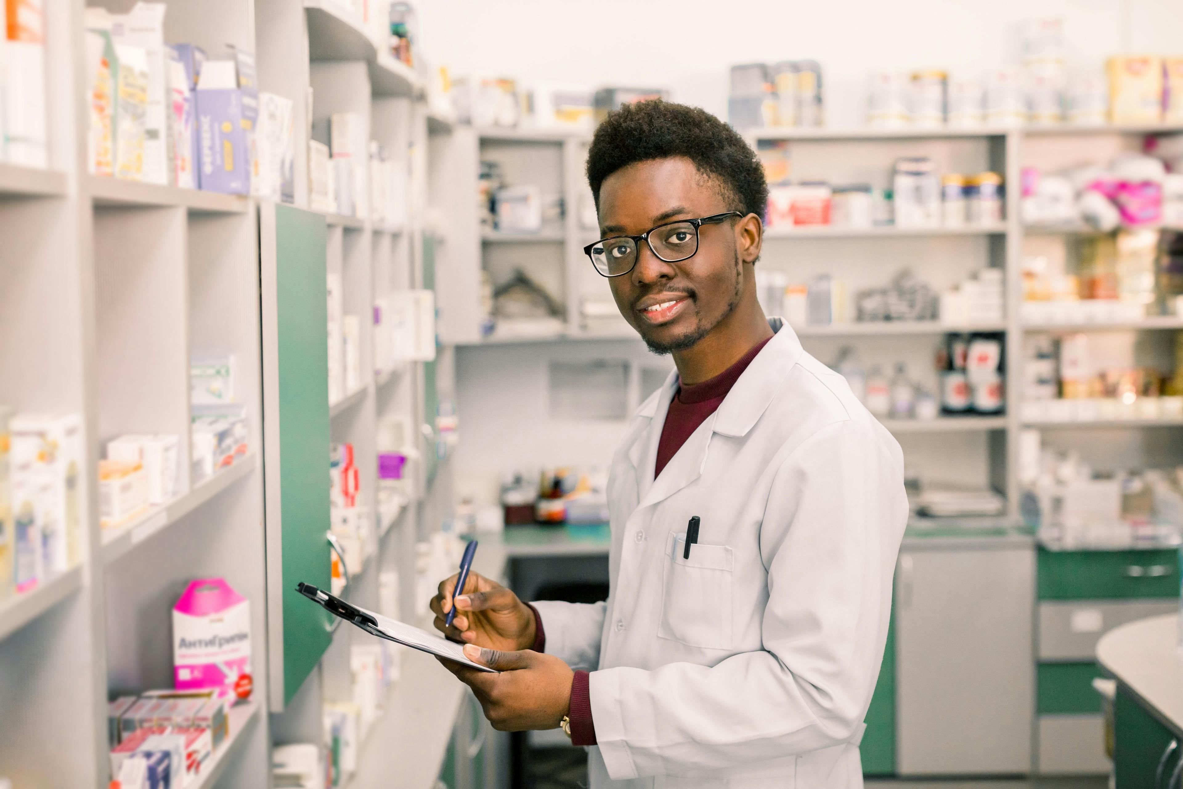 Smiling pharmacist technician looking at the camera and holding medications in the pharmacy