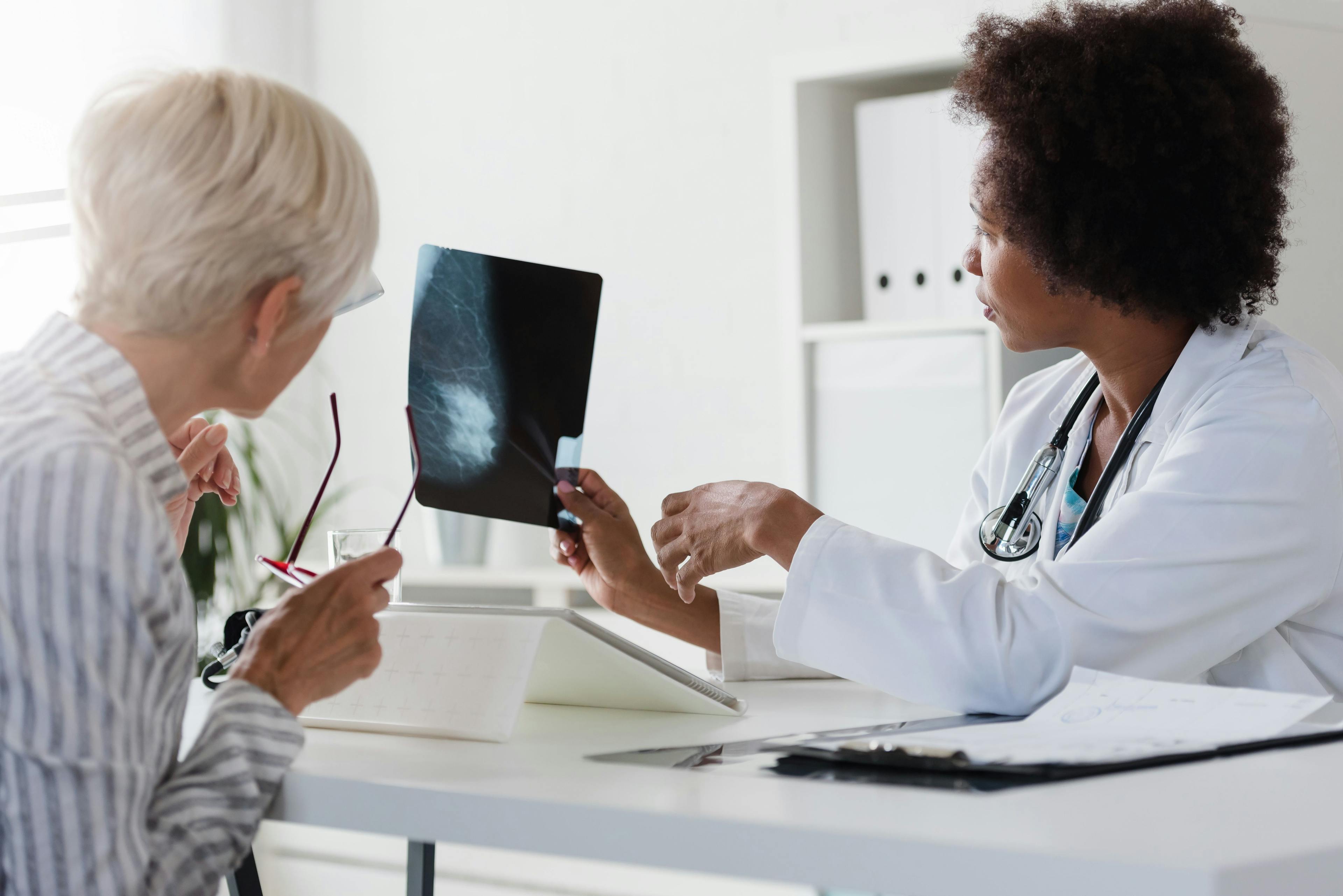 A female doctor sits at her desk and talks to a female patient while looking at her mammogram | Image Credit: lordn - stock.adobe.com