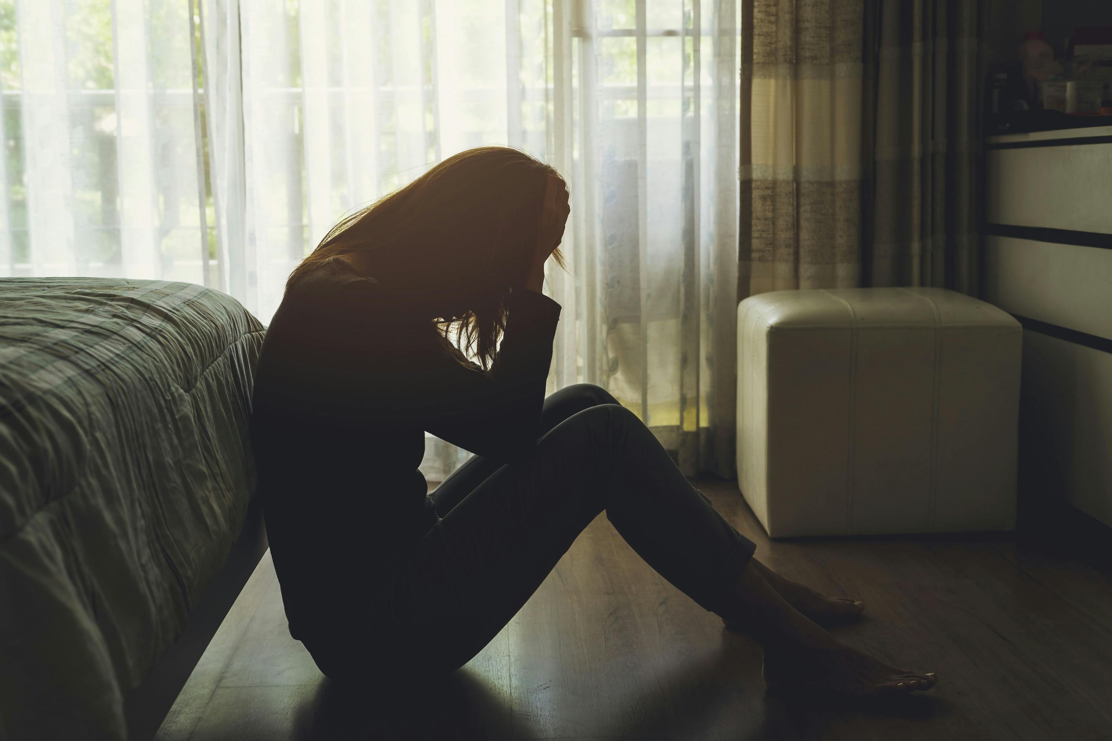 Lonely young woman feeling depressed and stressed sitting head in hands in the dark bedroom, Negative emotion and mental health concept | Image credit: Kittiphan - stock.adobe.com