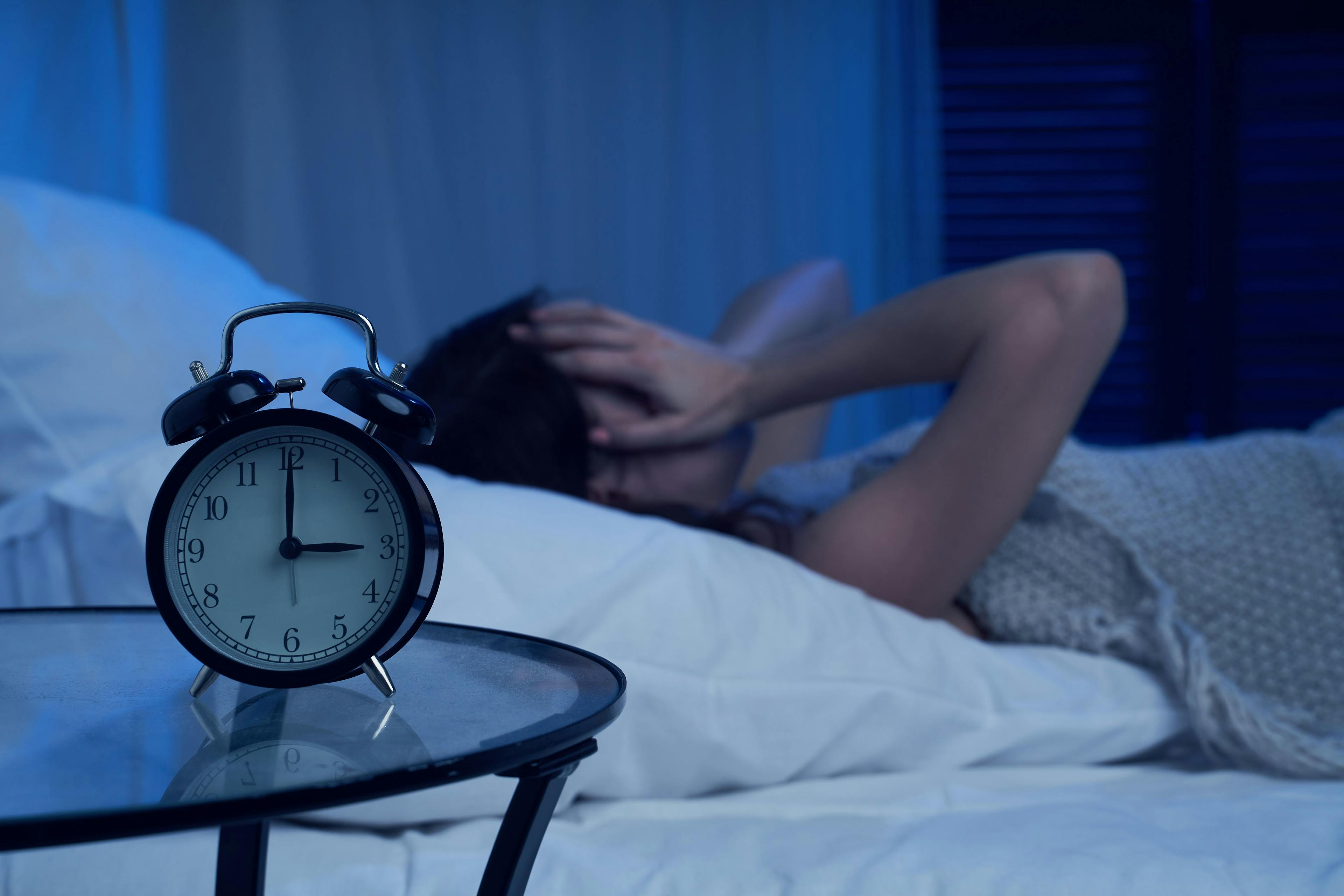 Image credit: Sergey | stock.adobe.com - Unhappy woman with insomnia lying on bed next to alarm clock at night