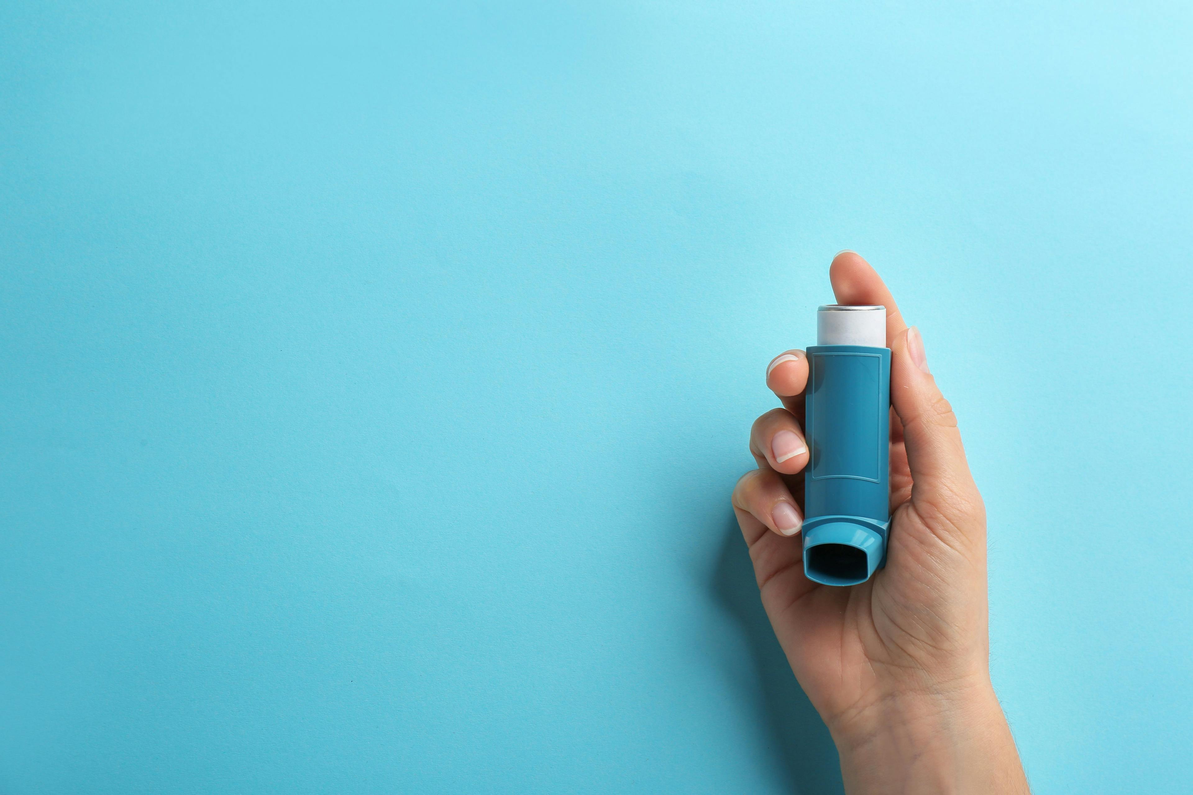 Woman holding asthma inhaler on color background, top view. | Image Credit: New Africa - stock.adobe.com