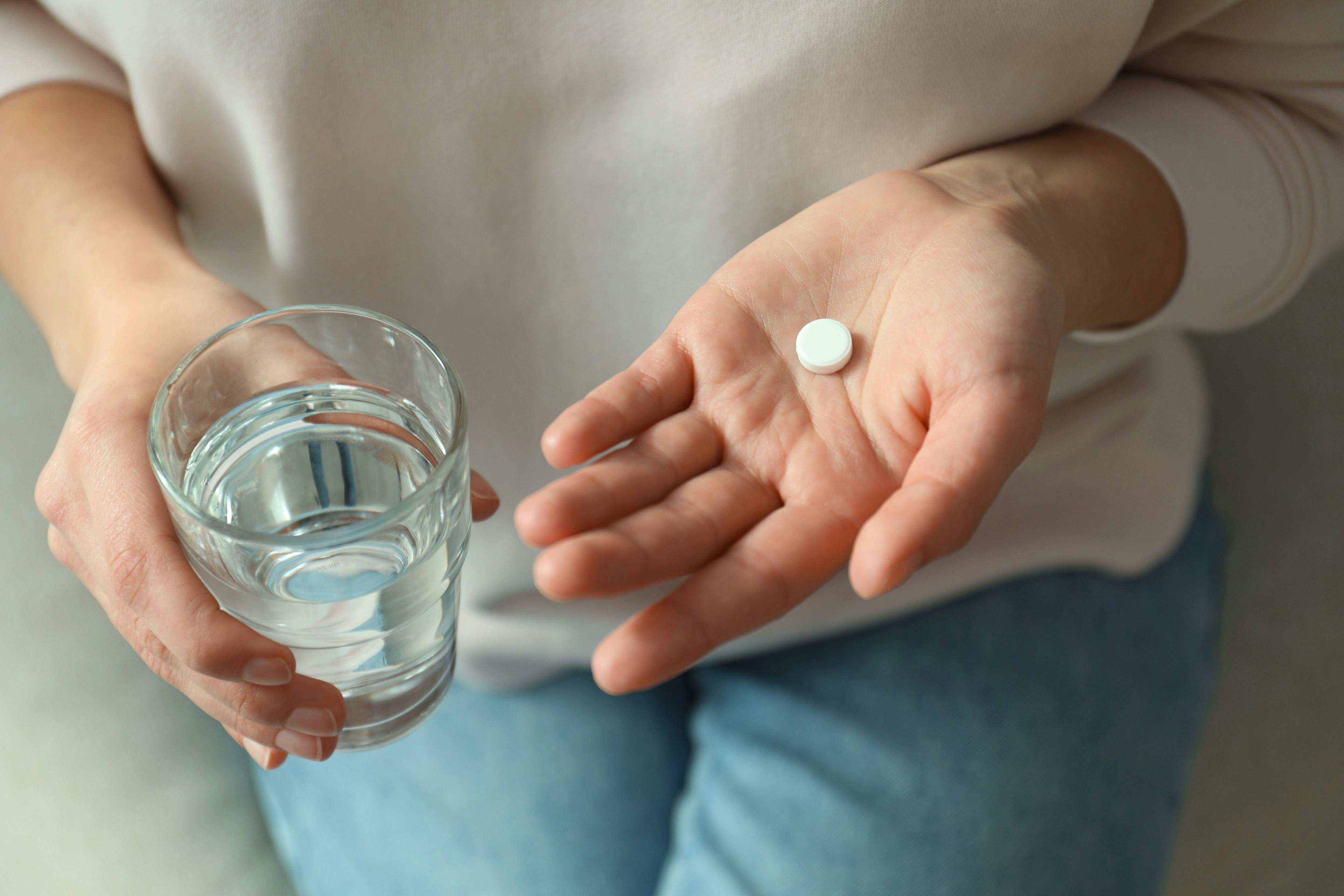 Woman holding a glass of water and a pill