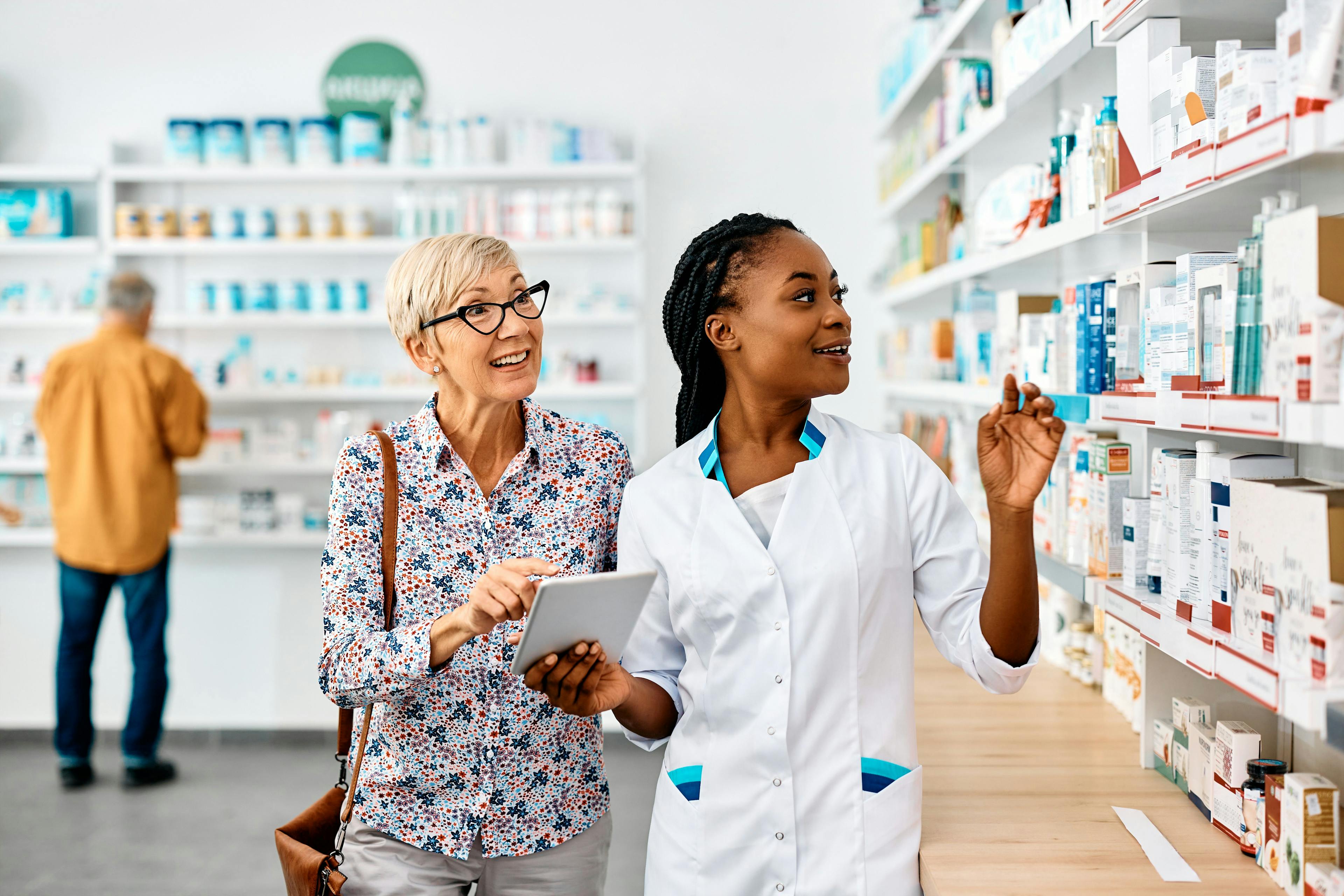 Young black pharmacist assists senior woman in buying medicine in pharmacy. | Image Credit: Drazen - stock.adobe.com